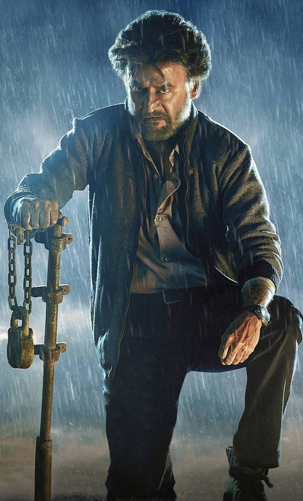 actor 桌布 壁紙 — 一個粗獷留鬚的男人在傾盆大雨中挑釁地站立，抓著一條被鏈條綁著的柱子，在戲劇性的藍色燈光下。