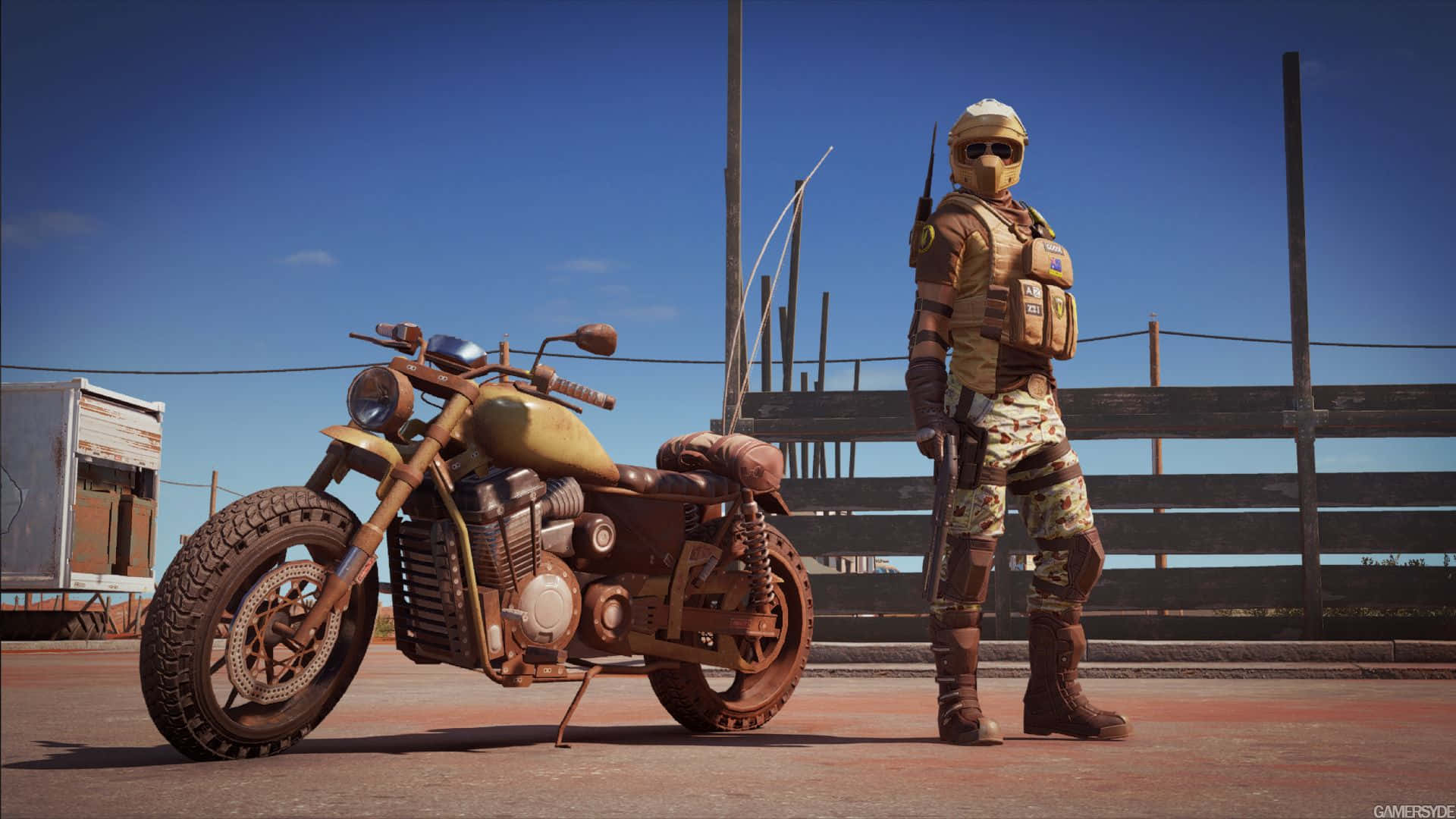 Rainbow Six Siege Mozzie 桌布 壁紙 — 一個粗獷的沙漠戰士站在一輛飽經風霜的機車旁，背景是晴朗的藍天和木柵欄。
