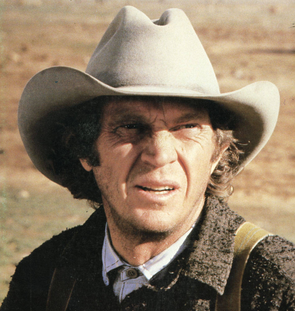 Cowboy 桌布 壁紙 — 一個粗獷的牛仔，臉龐飽經風霜，眼神銳利，戴著淺灰色帽子，背景是塵土飛揚的沙漠。