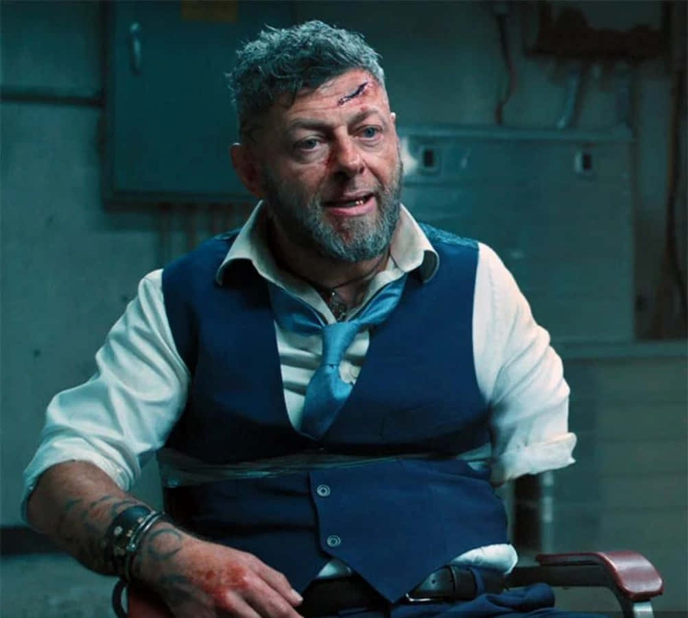 Ulysses Klaue 桌布 壁紙 — 一個粗獷的男人，額頭流血，手臂有刺青，被綁在昏暗工業房間的椅子上。