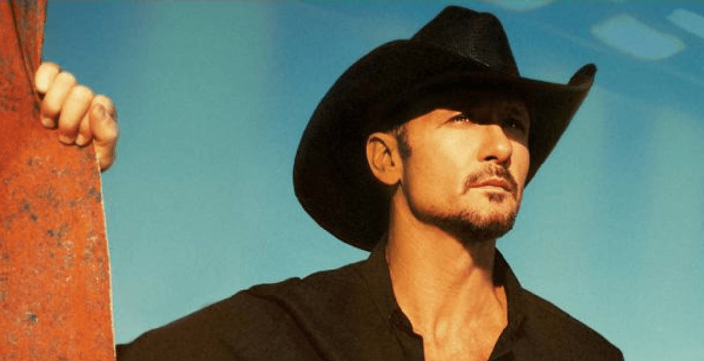 Tim Mcgraw 桌布 壁紙 — 一個粗獷的男人戴著黑色牛仔帽，在晴朗的藍天下抓住一根生鏽的金屬柱。
