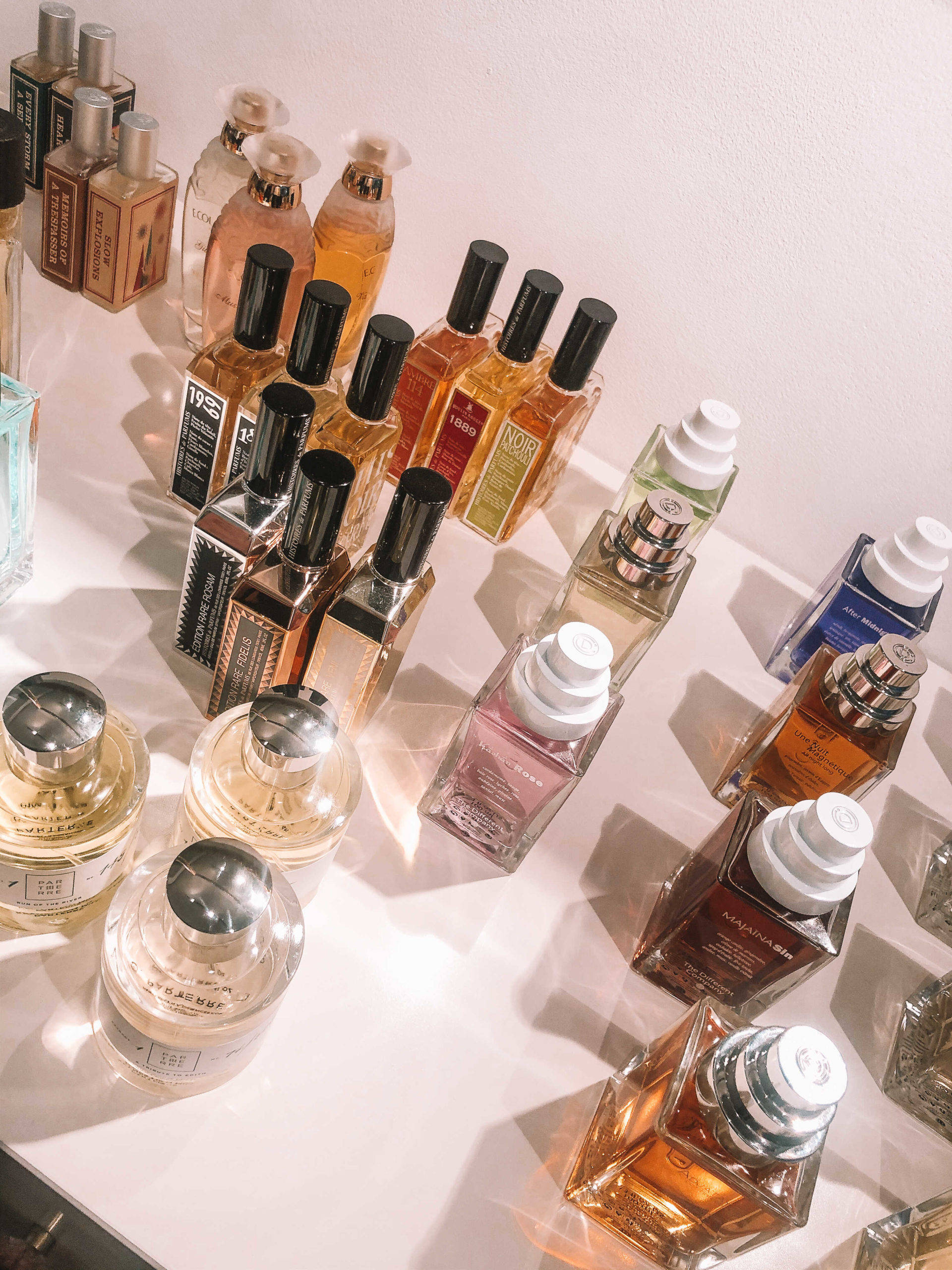 Chanel Aesthetic 桌布 壁紙 — 一個精心挑選的香水瓶系列，形狀各異，琥珀色調，在柔和陽光下排列在明亮的白色表面上。