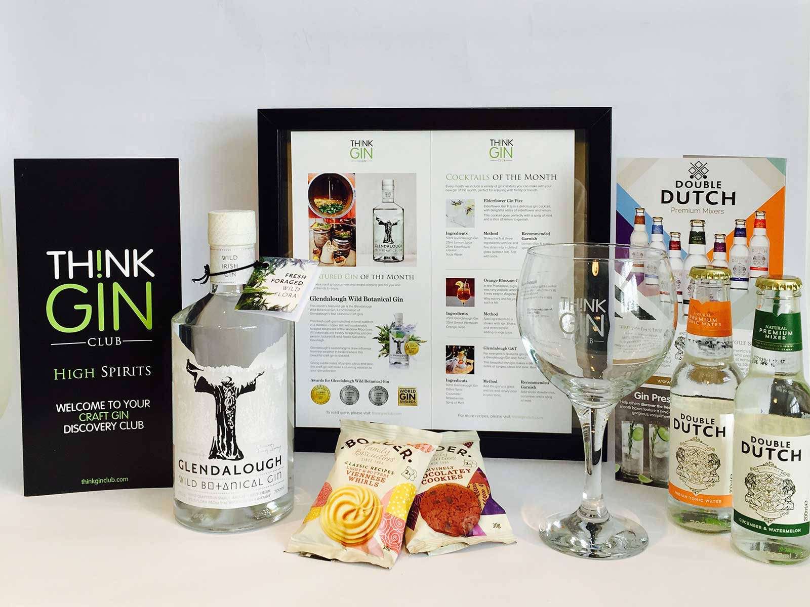 drinks 桌布 壁紙 — 一個精心策劃的琴酒訂閱盒展示，包含一大瓶格倫達洛琴酒、雞尾酒食譜、小吃和幾小瓶雙荷蘭琴酒，置於白色表面上。