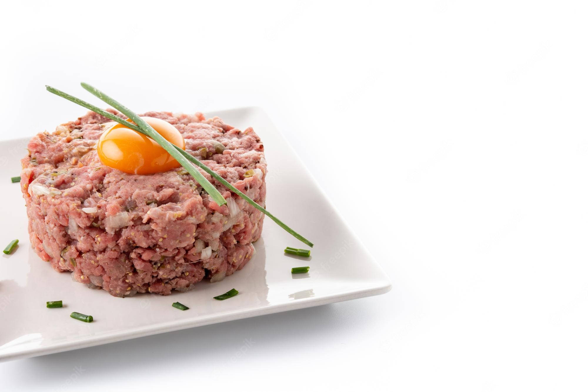 meat 桌布 壁紙 — 一個精心製作的牛肉塔塔堆，上面放著生蛋黃，並用細香蔥裝飾在白色盤子上。