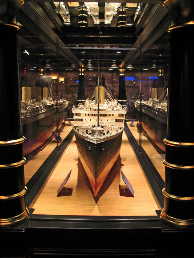 Museum 桌布 壁紙 — 一個精心製作的鐵達尼號模型，展示在一個帶有反光黑色柱子和溫暖環境照明的巨大玻璃陳列櫃中。