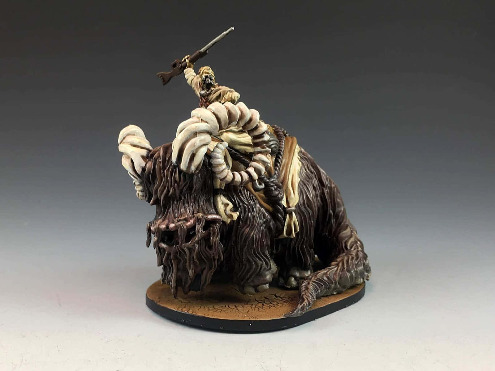 Bantha 桌布 壁紙 — 一個精細的微型人偶，騎在一隻長有獠牙的毛茸茸野獸上，手持步槍，背景為漸變灰色。