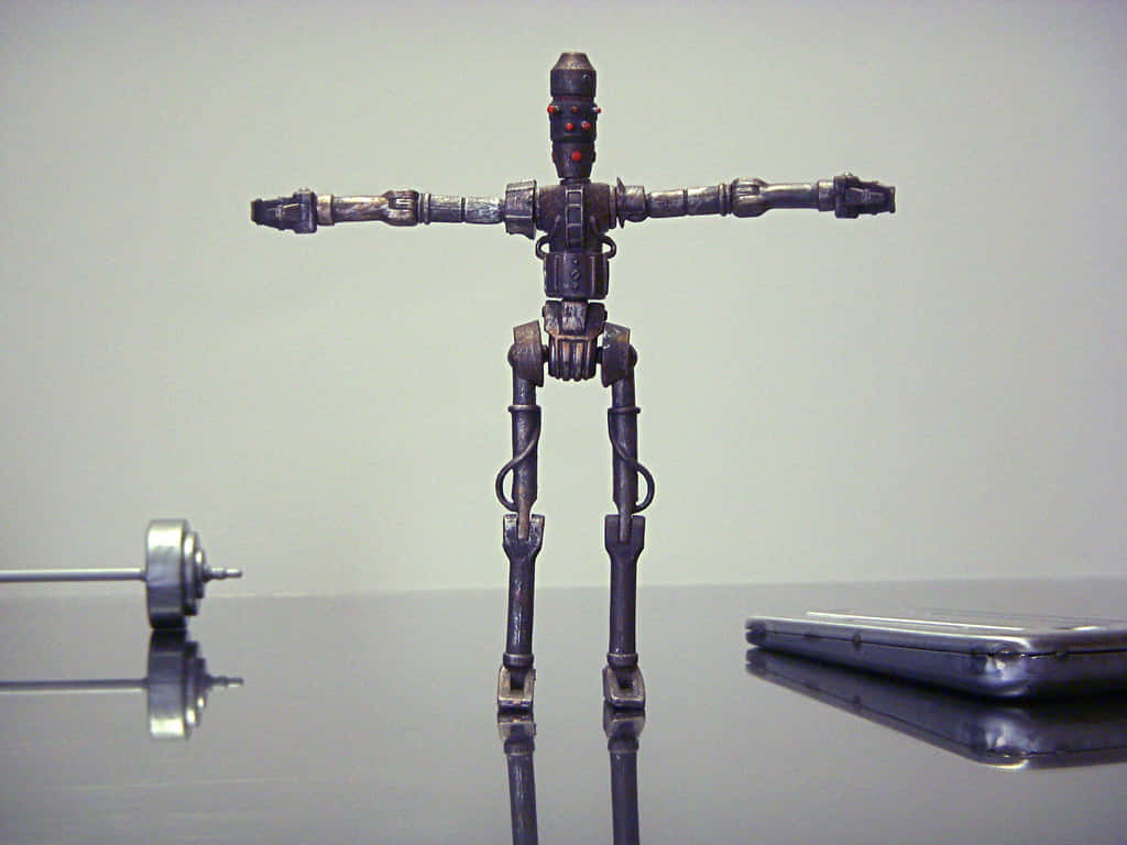 Ig-88 桌布 壁紙 — 一個精細的金屬機器人公仔站在反光表面上，雙臂伸展，旁邊有一個啞鈴和智慧型手機。