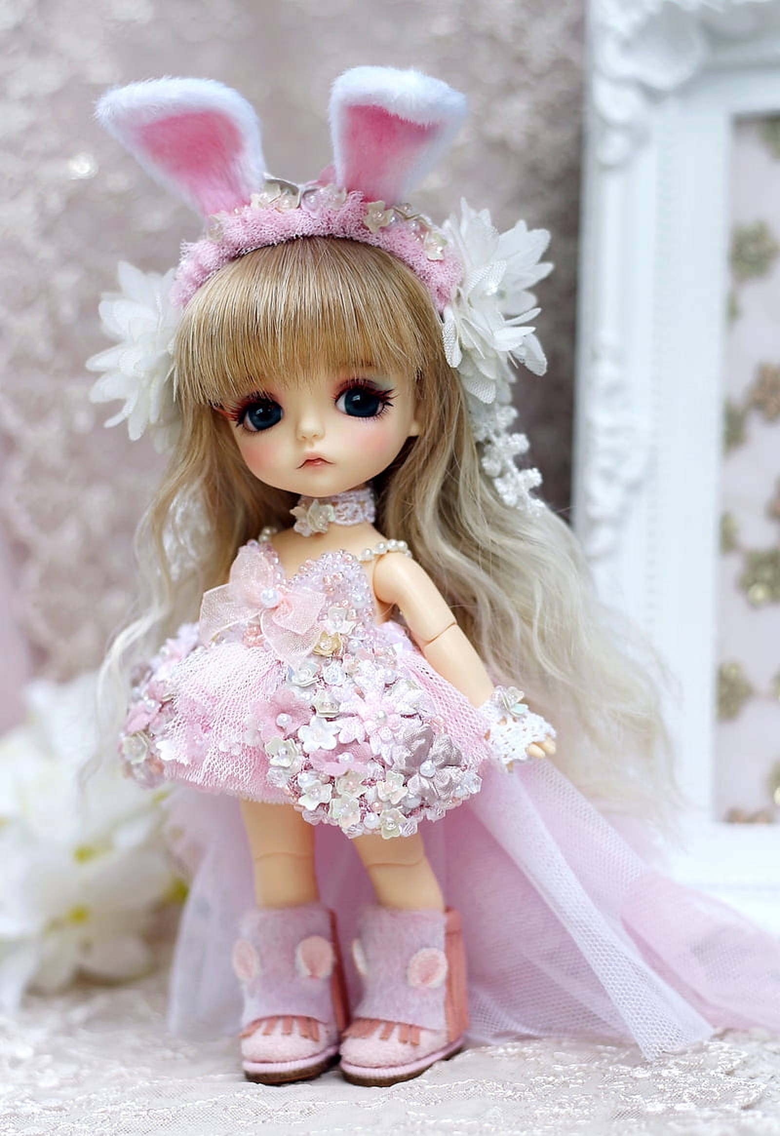 Doll 桌布 壁紙 — 一個精緻的bjd娃娃，戴著兔耳朵和花卉粉紅色連衣裙，在柔軟的蕾絲背景下優雅地站立。