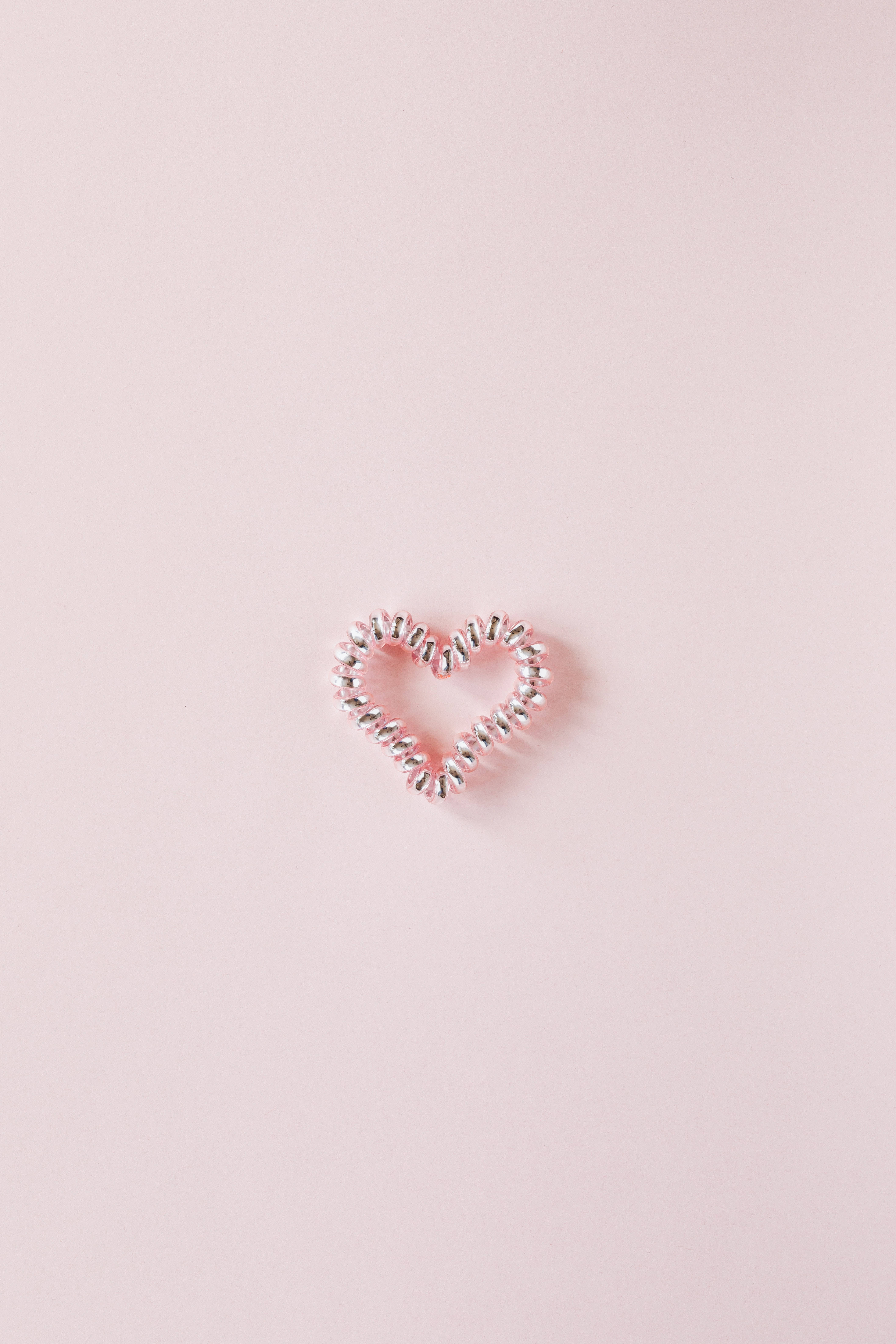Pastel Pink Heart 桌布 壁紙 — 一個精緻的心形髮圈，由鍍銀珠子製成，置於柔軟的粉紅色背景中央。
