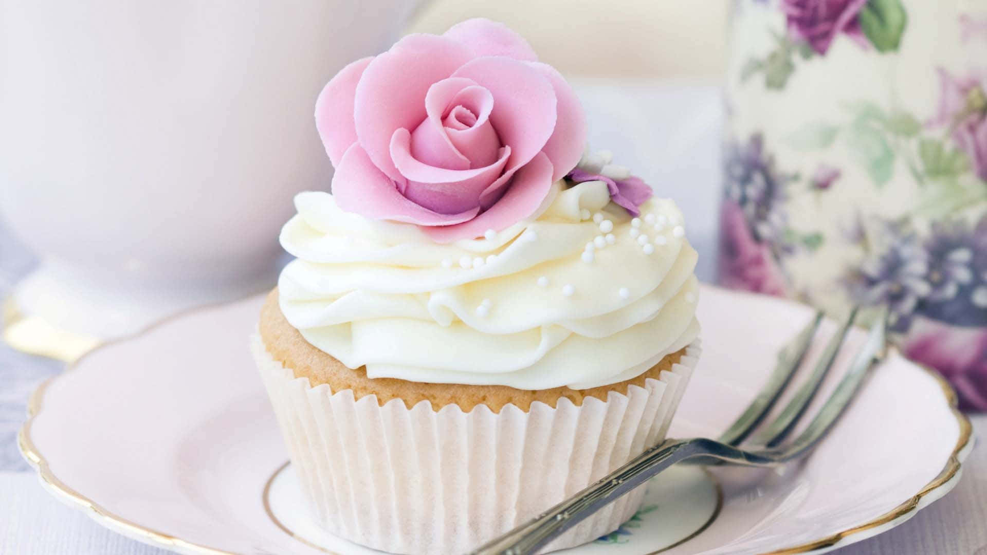 Cupcake 桌布 壁紙 — 一個精緻的杯子蛋糕，上面有粉紅色糖玫瑰和珍珠糖粒，放在復古花卉盤子上，旁邊有叉子。