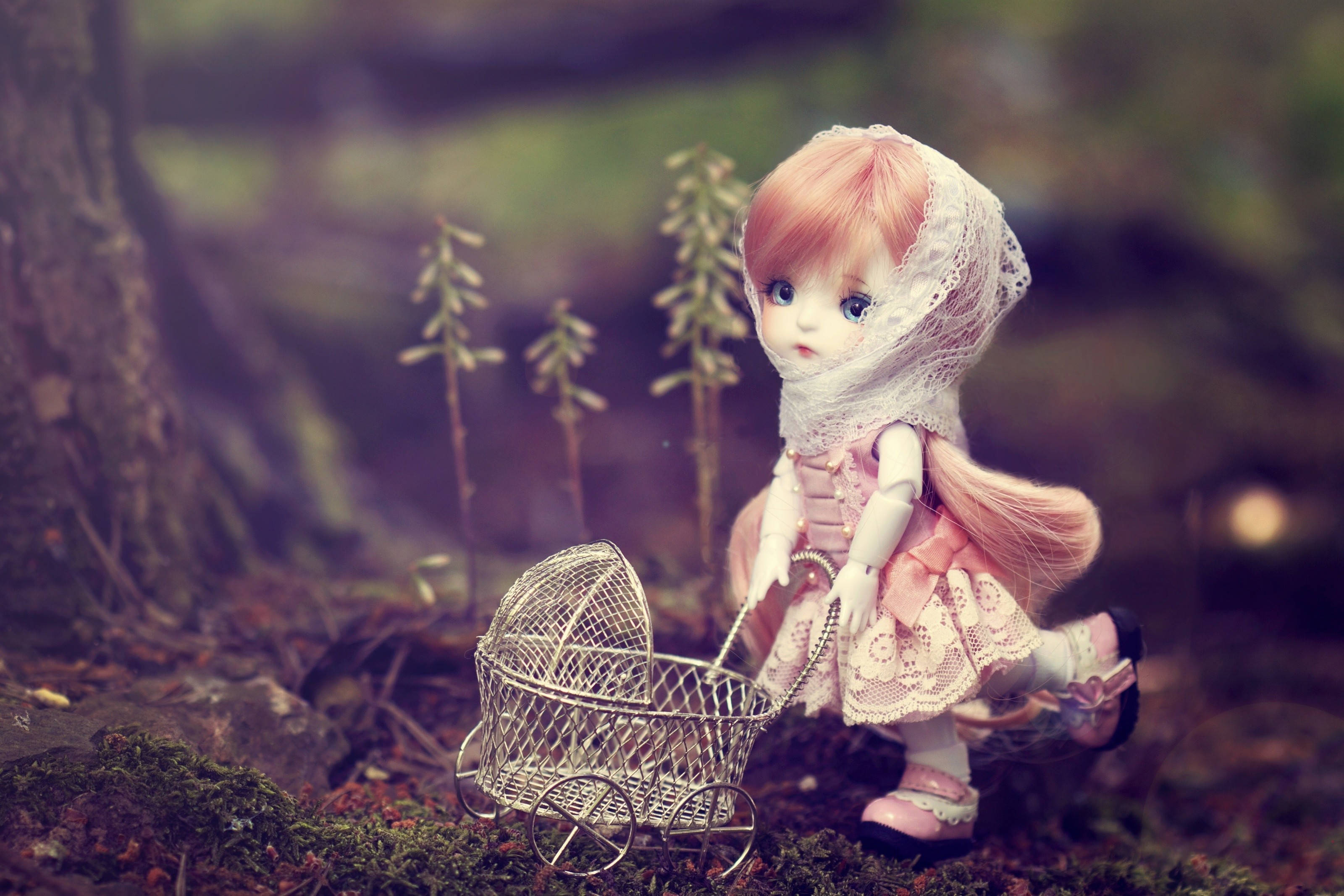 Barbie Doll 桌布 壁紙 — 一個精緻的洋娃娃，粉紅色頭髮和蕾絲面紗，推著一個細小的鐵絲嬰兒車穿過長滿苔蘚的森林地面。