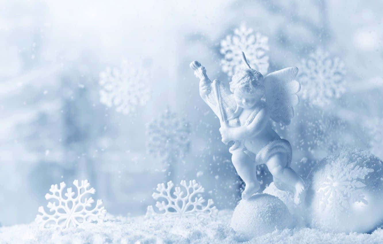Snow Angel 桌布 壁紙 — 一個精緻的白色天使雕像在飄落的雪花和被雪覆蓋的裝飾品中吹奏小號，營造出寒冷的冬季場景。