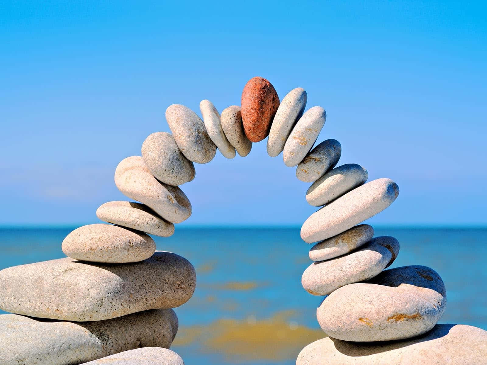Stone 桌布 壁紙 — 一個精緻的石拱門平衡地放在沙灘上，背後是碧綠色的海洋和清澈的藍天。