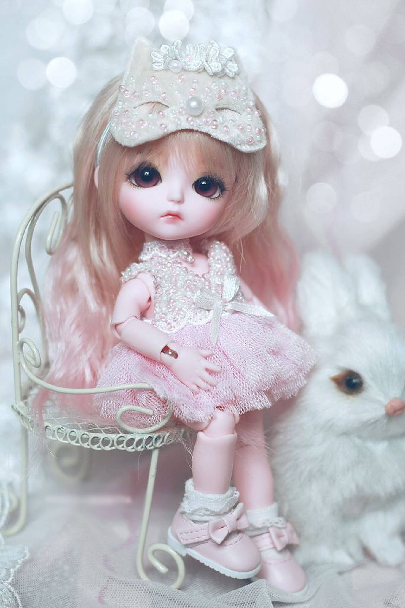 Doll 桌布 壁紙 — 一個精緻的粉紅色 Blythe 娃娃，戴著珍珠裝飾的皇冠，坐在白色椅子上，旁邊有一隻毛茸茸的白色兔子，背景是閃爍的散景。