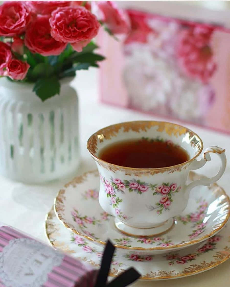 tea 桌布 壁紙 — 一個精緻的花卉茶杯，裝滿了深色茶，放在柔軟的白色表面上，旁邊是一個粉紅玫瑰花瓶。