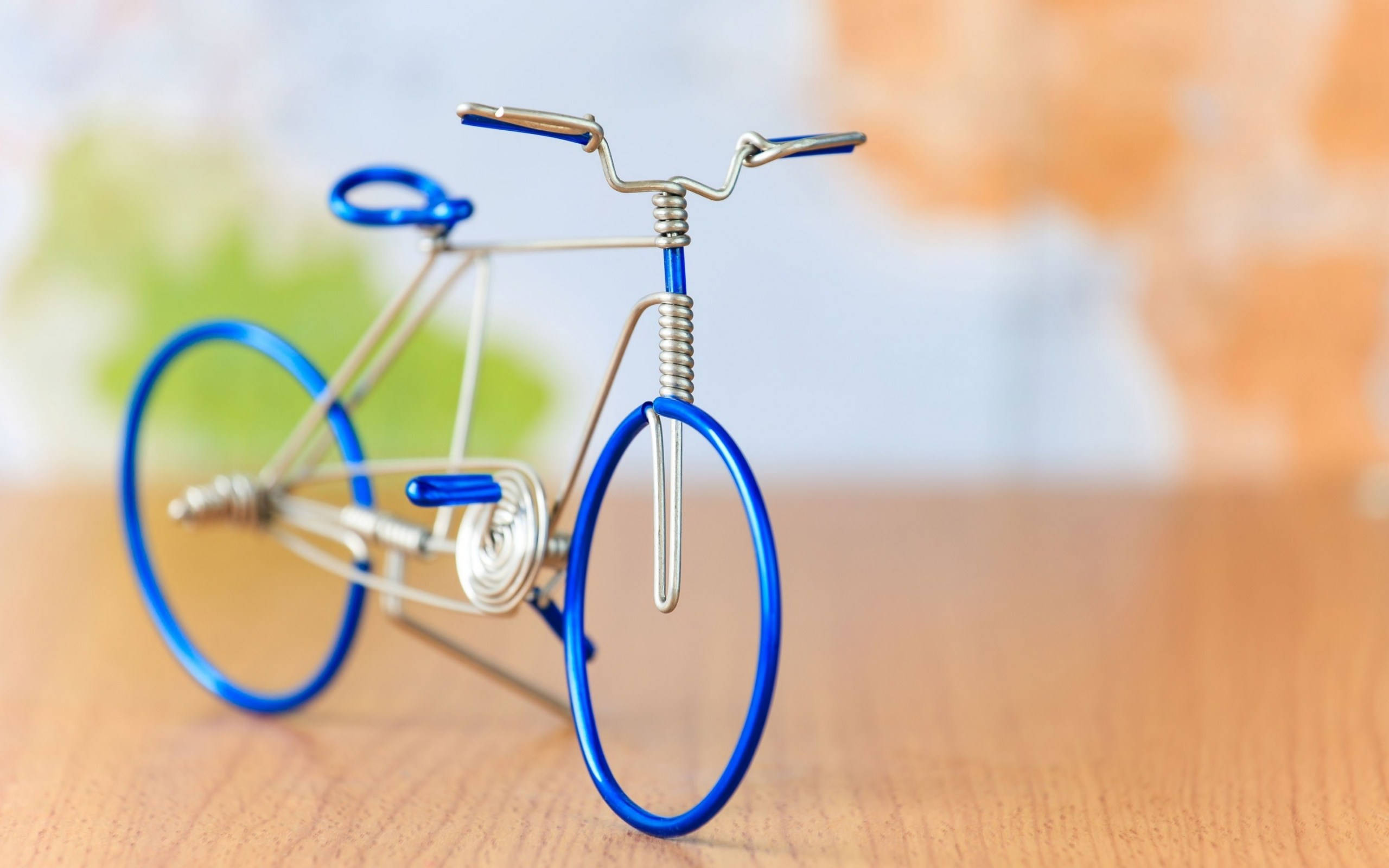 Bicycle 桌布 壁紙 — 一個精緻的鐵線腳踏車雕塑，藍色車輪，放在木質表面上，背景是柔和模糊的彩色。