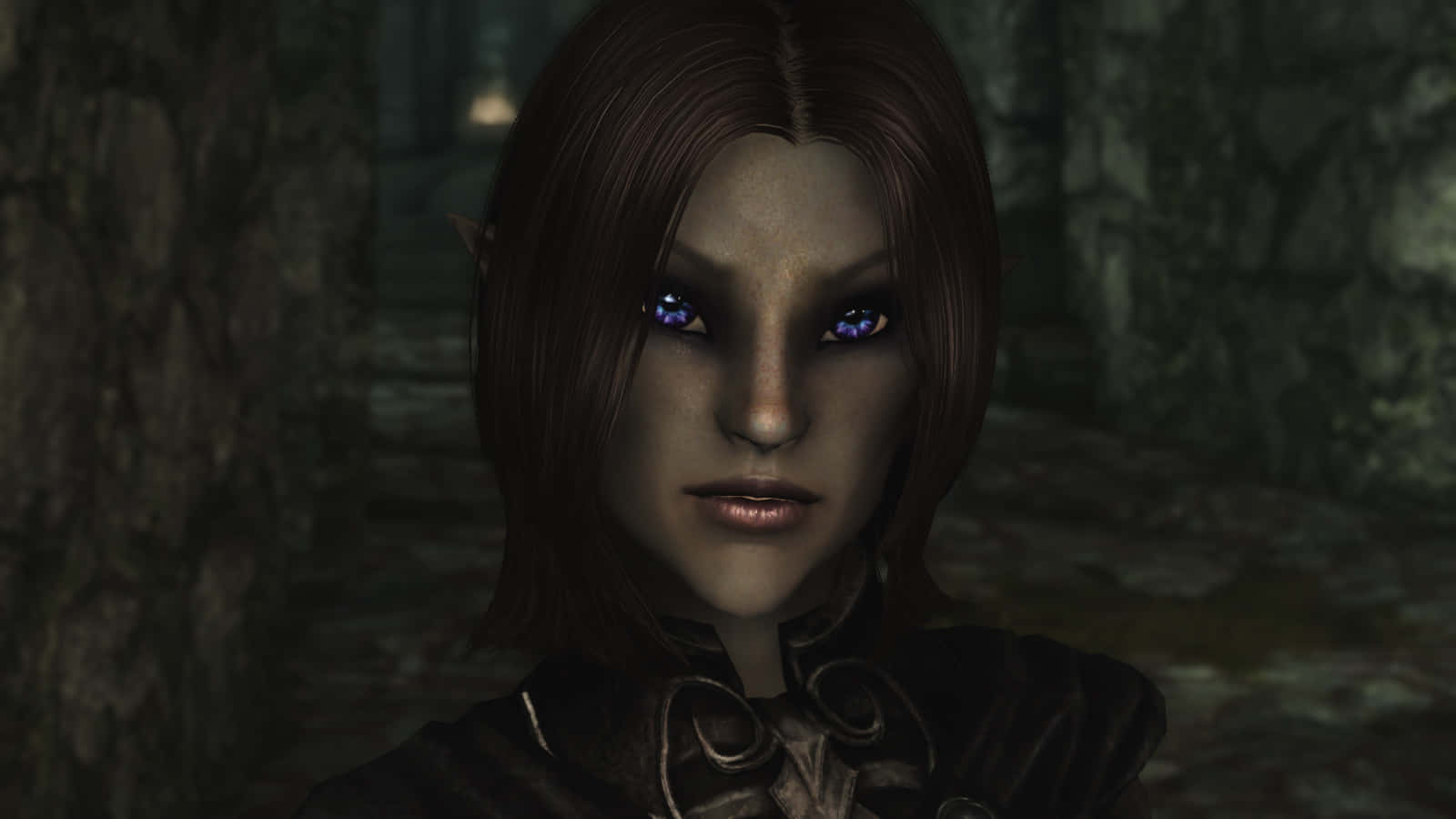 Skyrim Karliah 桌布 壁紙 — 一個精靈的近距離特寫，擁有發光的藍色眼睛和深色頭髮，站在昏暗的森林空地中。
