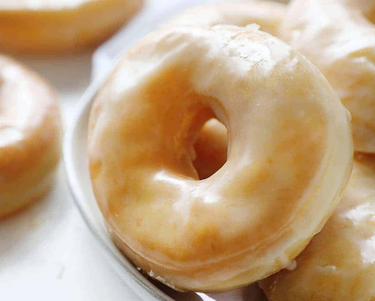 Glazed Donut 桌布 壁紙 — 一個糖霜甜甜圈的近距離特寫，帶有光澤的糖衣，放在白色盤子上。