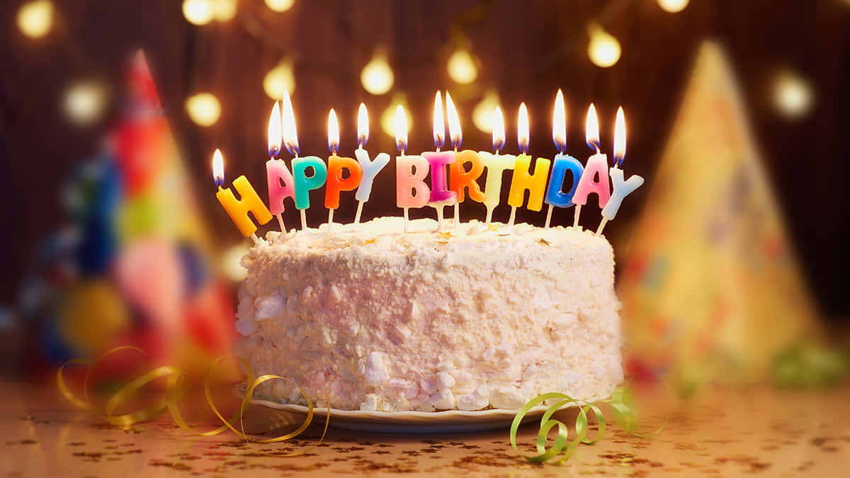 Fall Birthday 桌布 壁紙 — 一個糖霜生日蛋糕，上面有色彩繽紛的字母蠟燭拼出「HAPPY BIRTHDAY」，在溫暖的散景背景下閃爍著火焰。