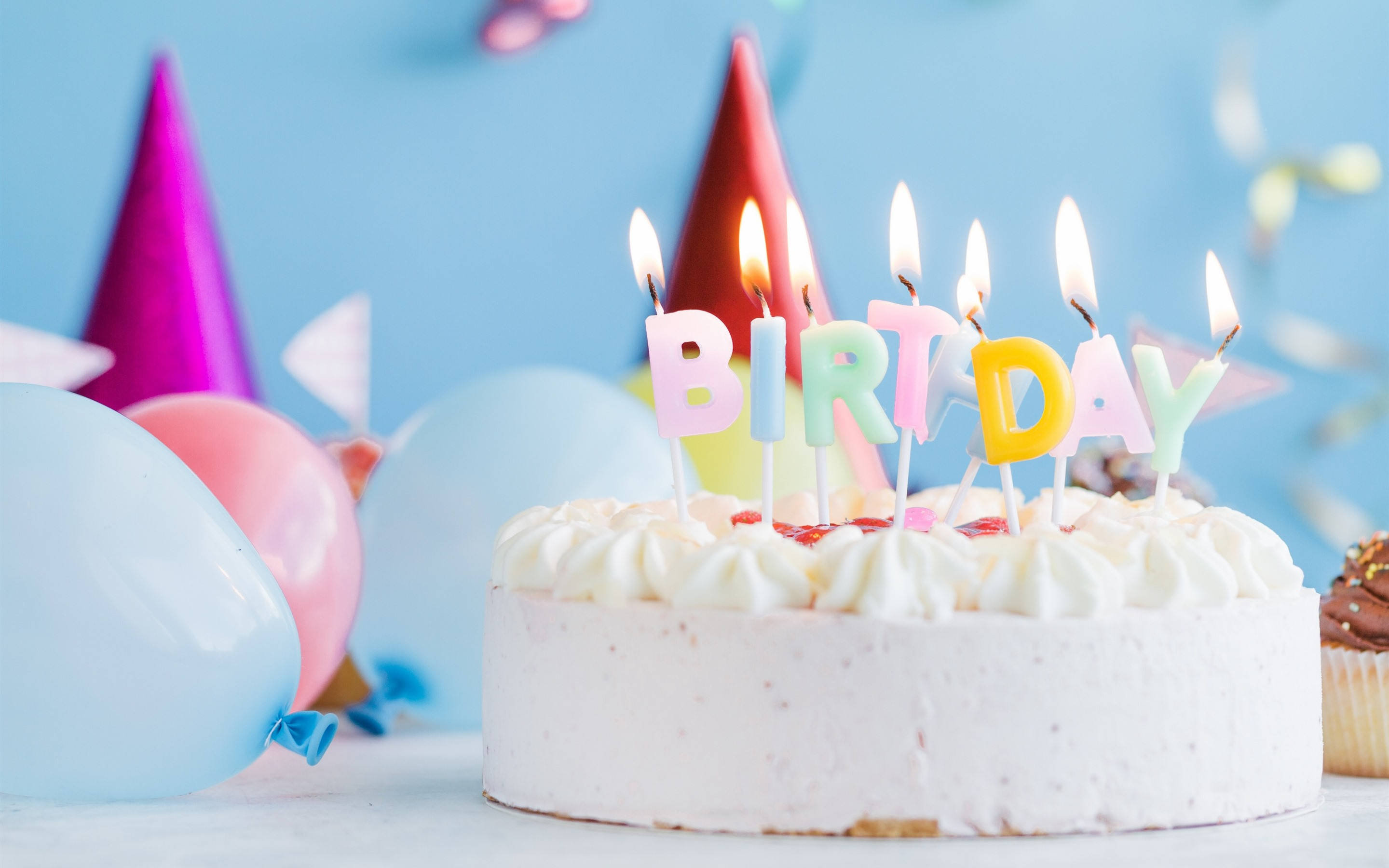 蛋糕 桌布 壁紙 — 一個糖霜生日蛋糕，頂部插著彩色「BIRTHDAY」蠟燭，周圍環繞著派對氣球，背景是柔和的藍色。