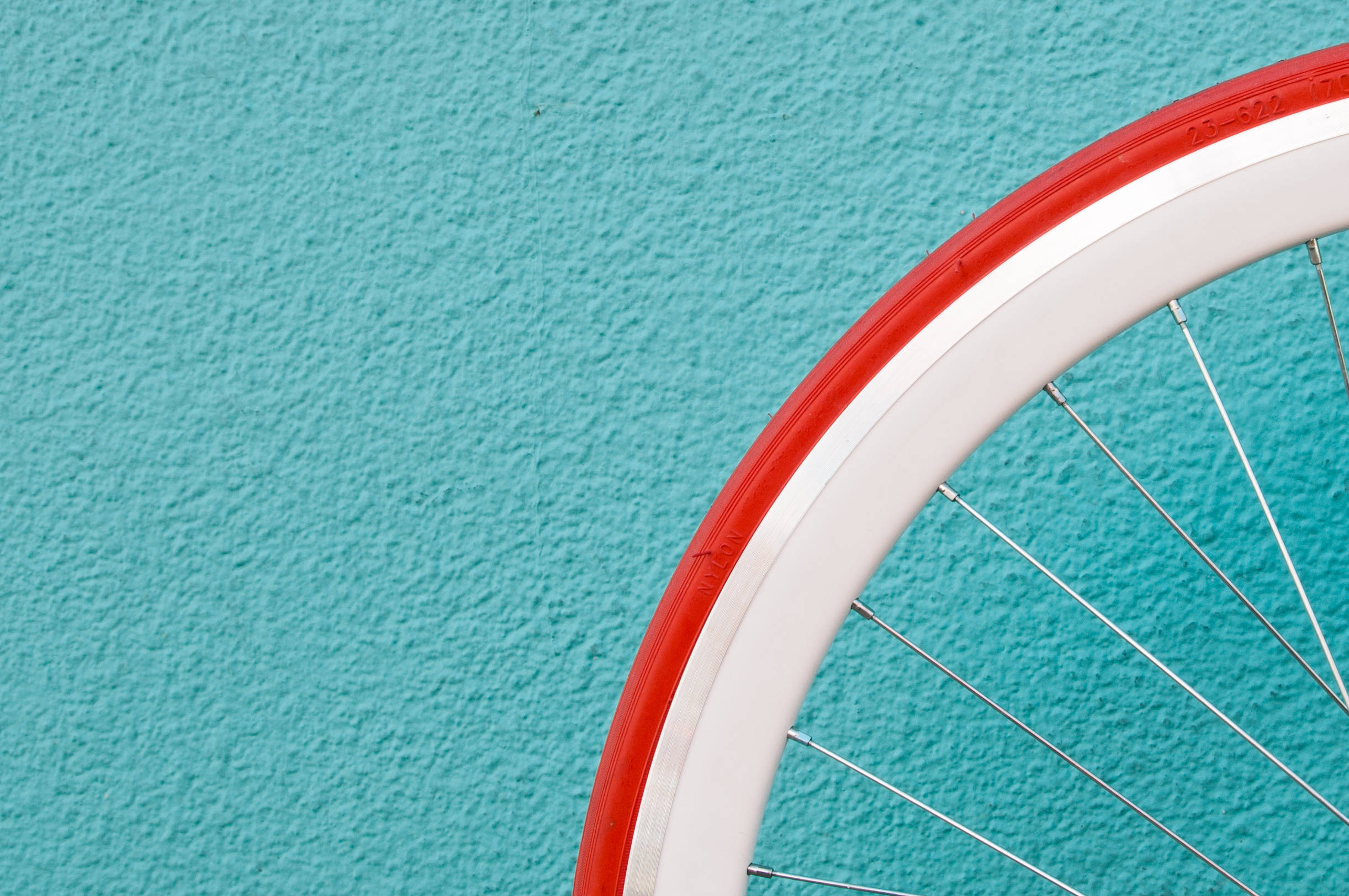 Bicycle 桌布 壁紙 — 一個紅白相間的自行車輪特寫，背景是帶紋理的青綠色牆壁。