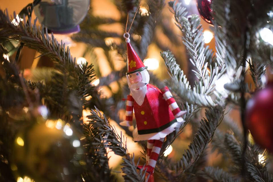 Santa Claus 桌布 壁紙 — 一個紅白色的木製精靈裝飾品掛在灑滿雪花的松樹枝上，被溫暖的仙女燈照亮。