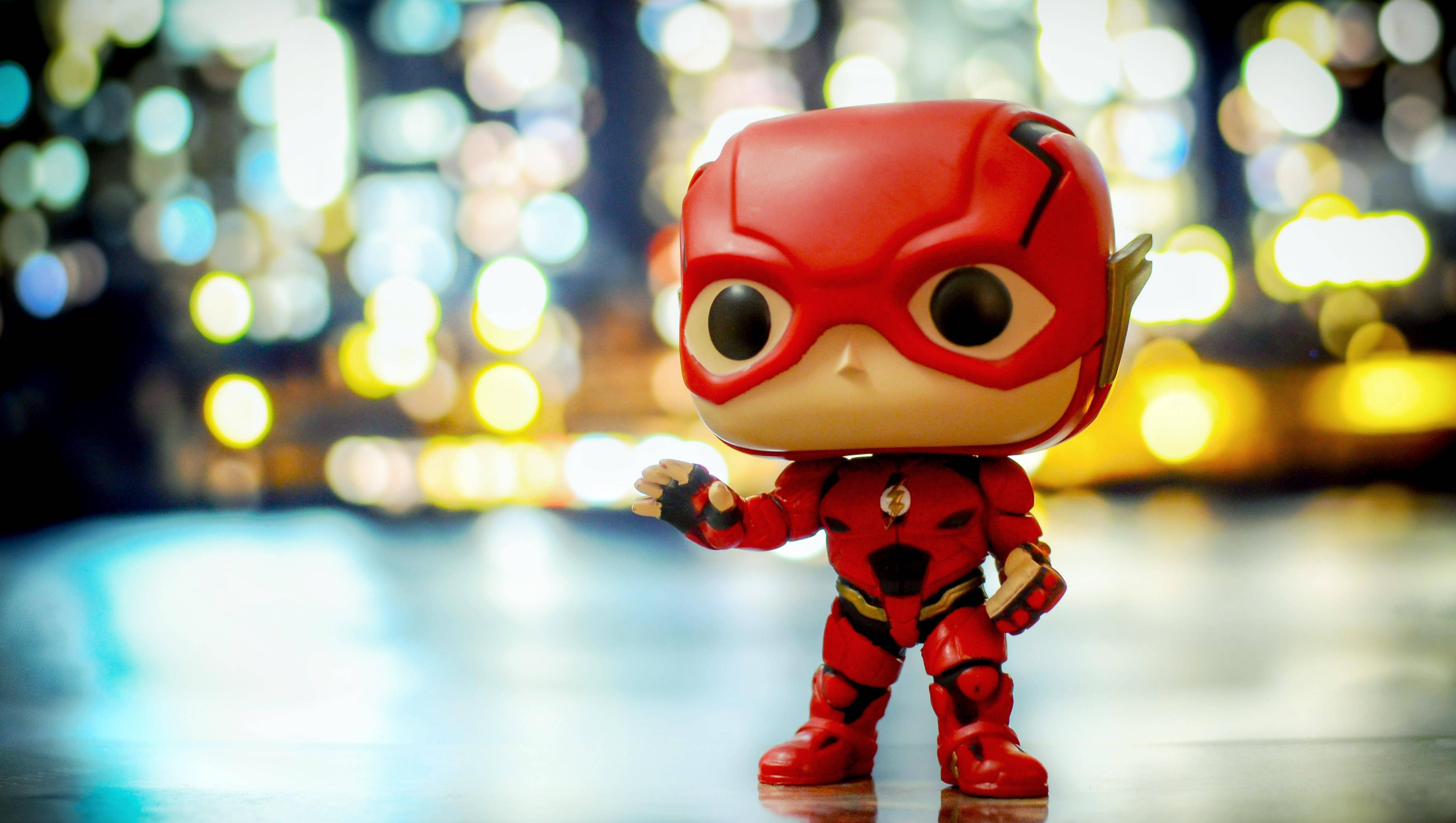 pop 桌布 壁紙 — 一個紅色Flash Funko Pop公仔自信地站在反光表面上，背景是充滿活力的散景城市夜景。
