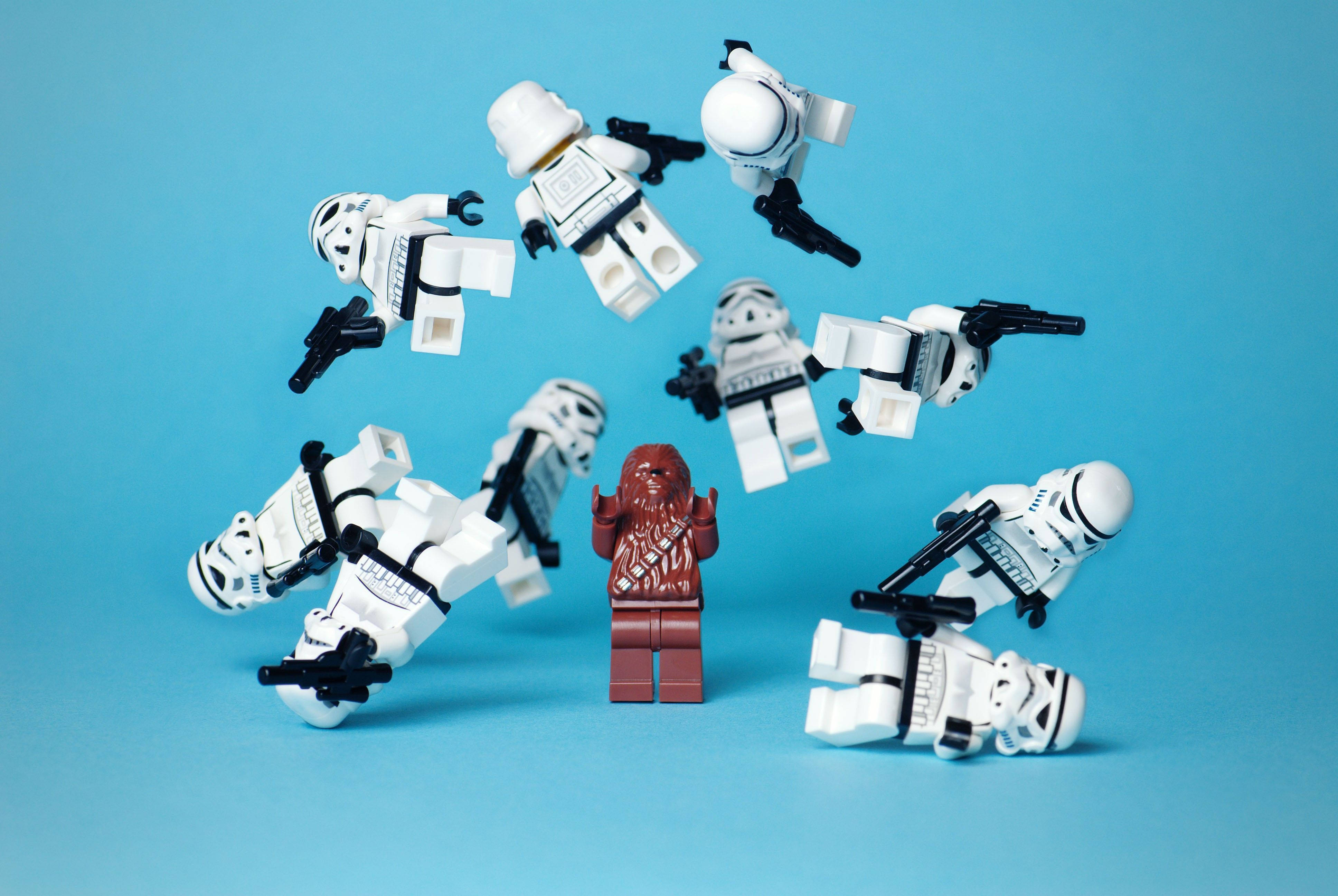 星際大戰 桌布 壁紙 — 一個紅色LEGO Chewbacca挑釁地站立，而白色LEGO Stormtroopers似乎在他周圍爆炸，背景為純藍色。