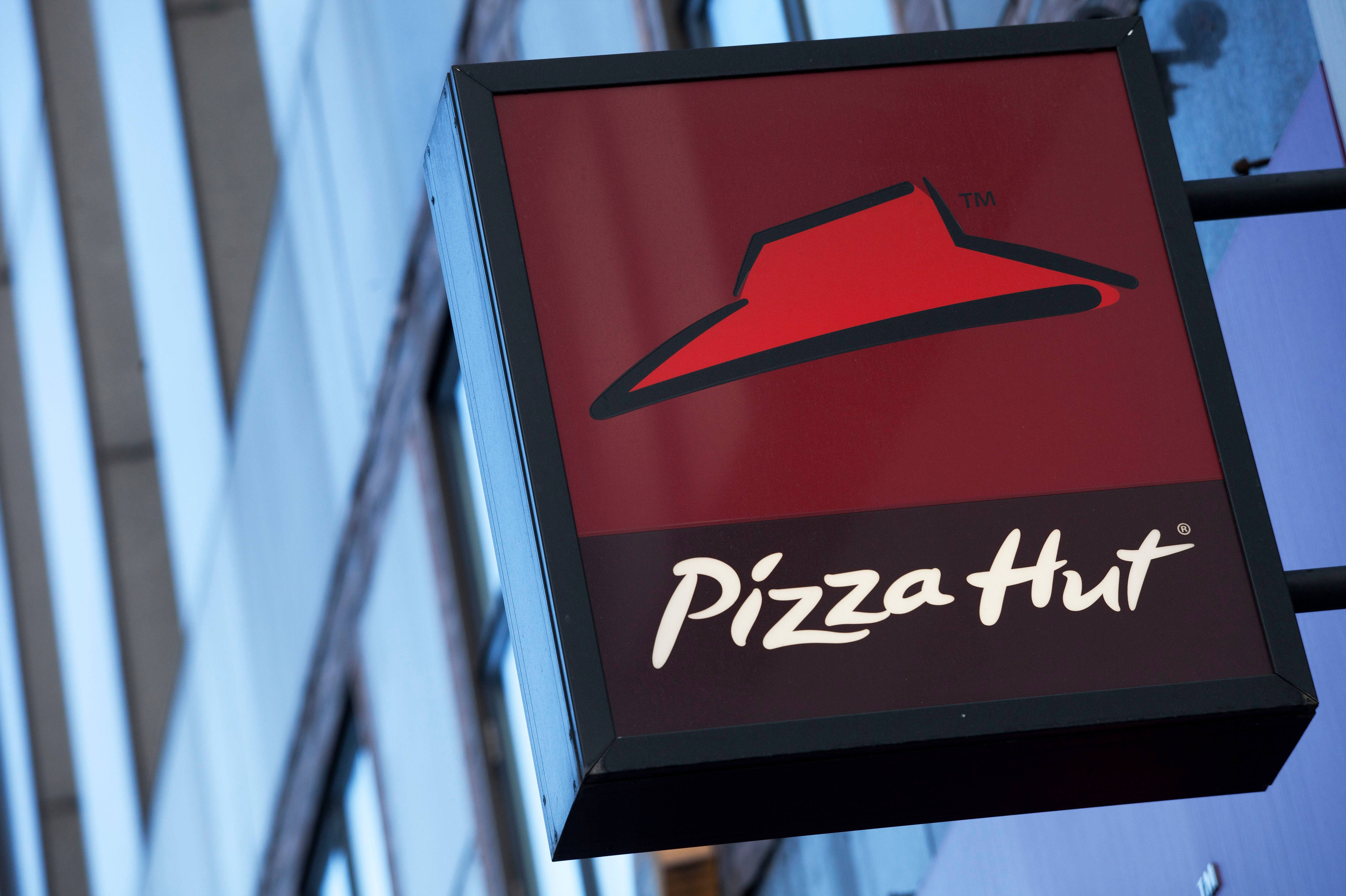 Hut 桌布 壁紙 — 一個紅色Pizza Hut標誌的特寫，帶有黑色邊框，掛在現代玻璃建築外牆上。