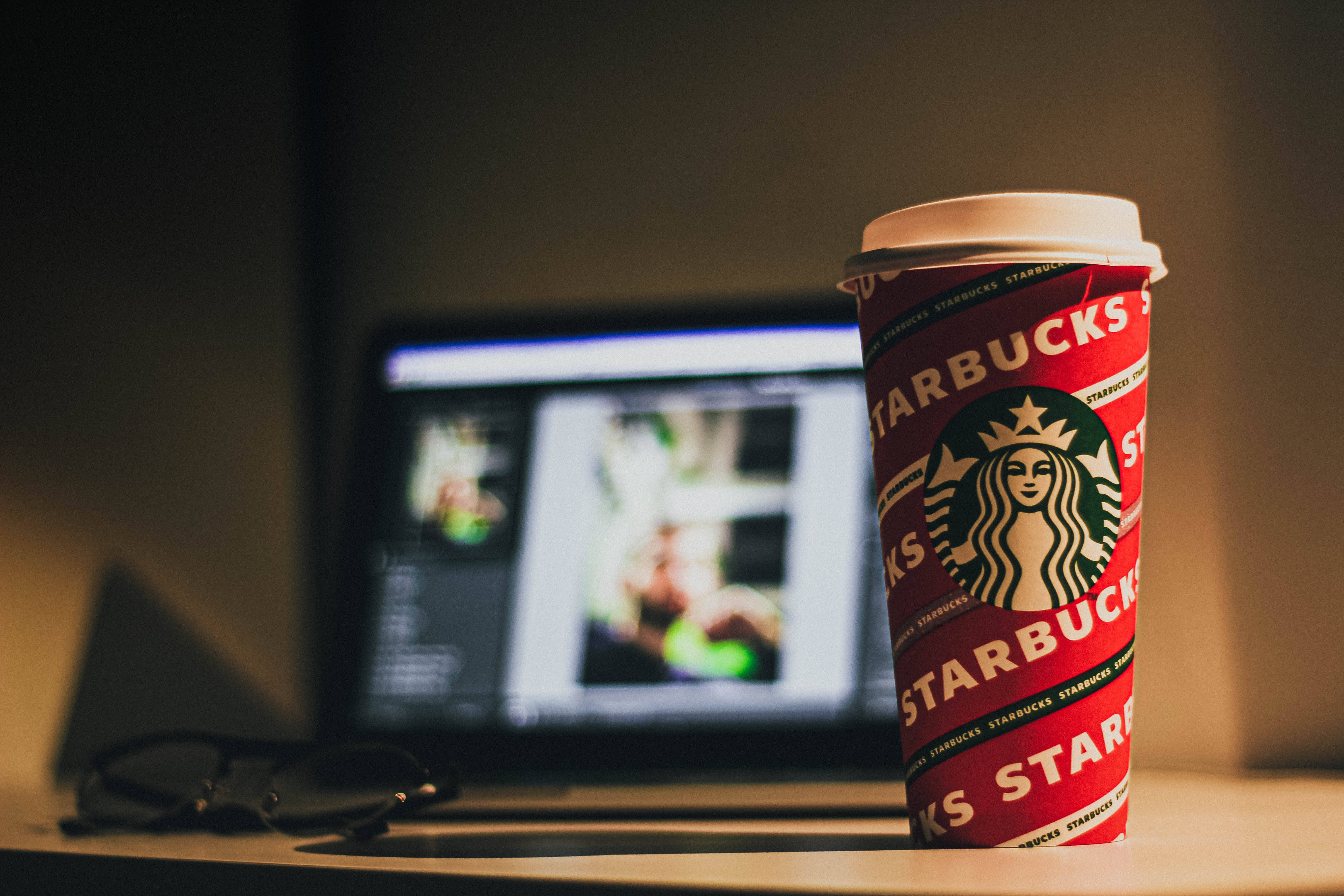 Editing 桌布 壁紙 — 一個紅色Starbucks咖啡杯放在溫暖光線下的桌上，旁邊有筆記型電腦和眼鏡。