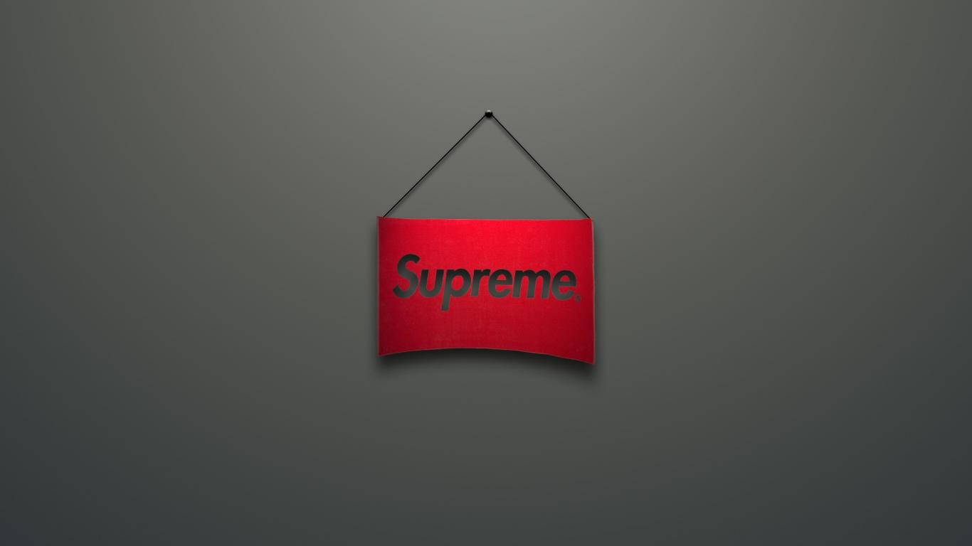 supreme 桌布 壁紙 — 一個紅色Supreme品牌標誌居中懸掛在深灰色牆壁上，柔和燈光投射出細微陰影。