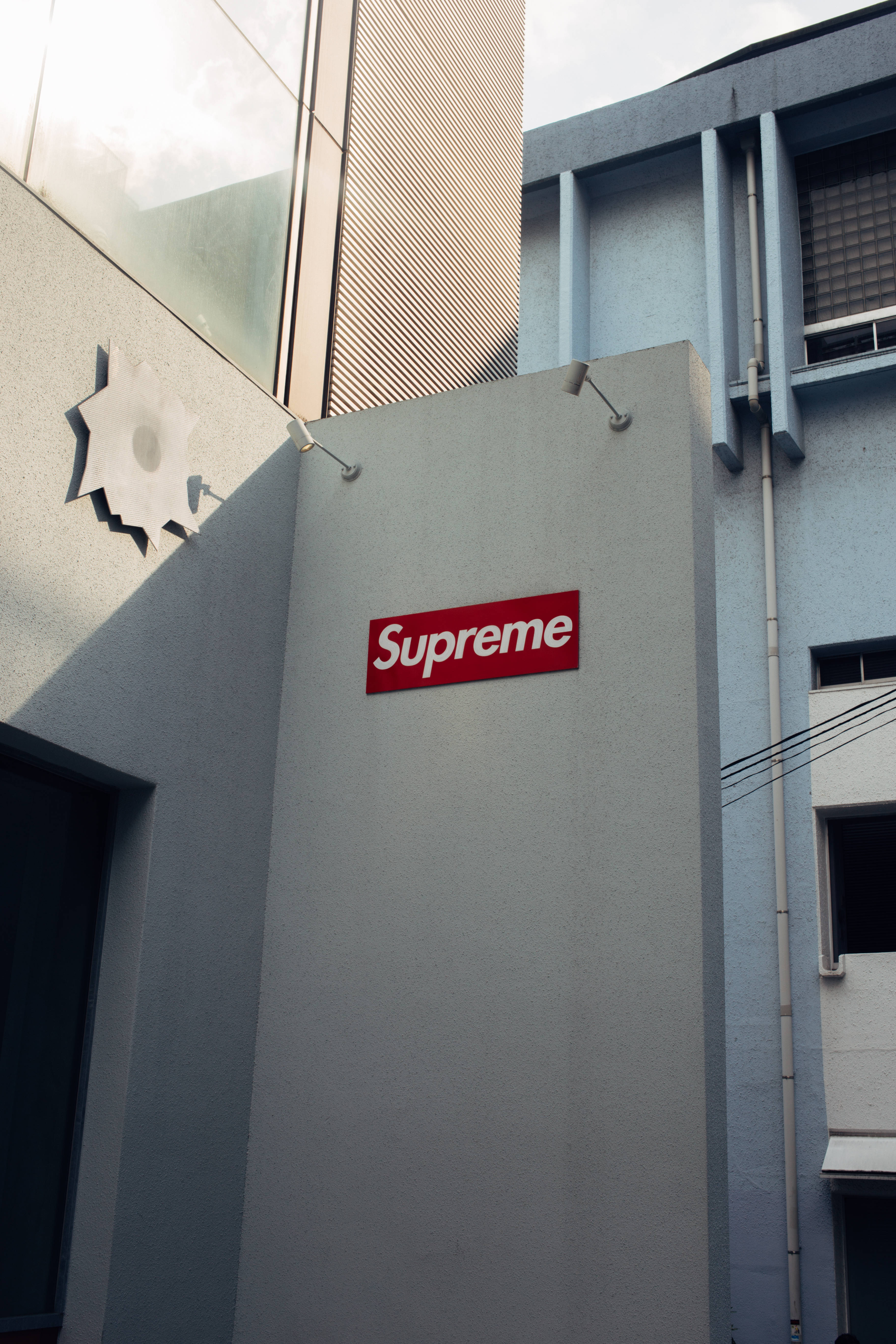 strange supreme 桌布 壁紙 — 一個紅色Supreme標誌牌安裝在現代城市建築的灰色混凝土牆上，在明亮的日光下。
