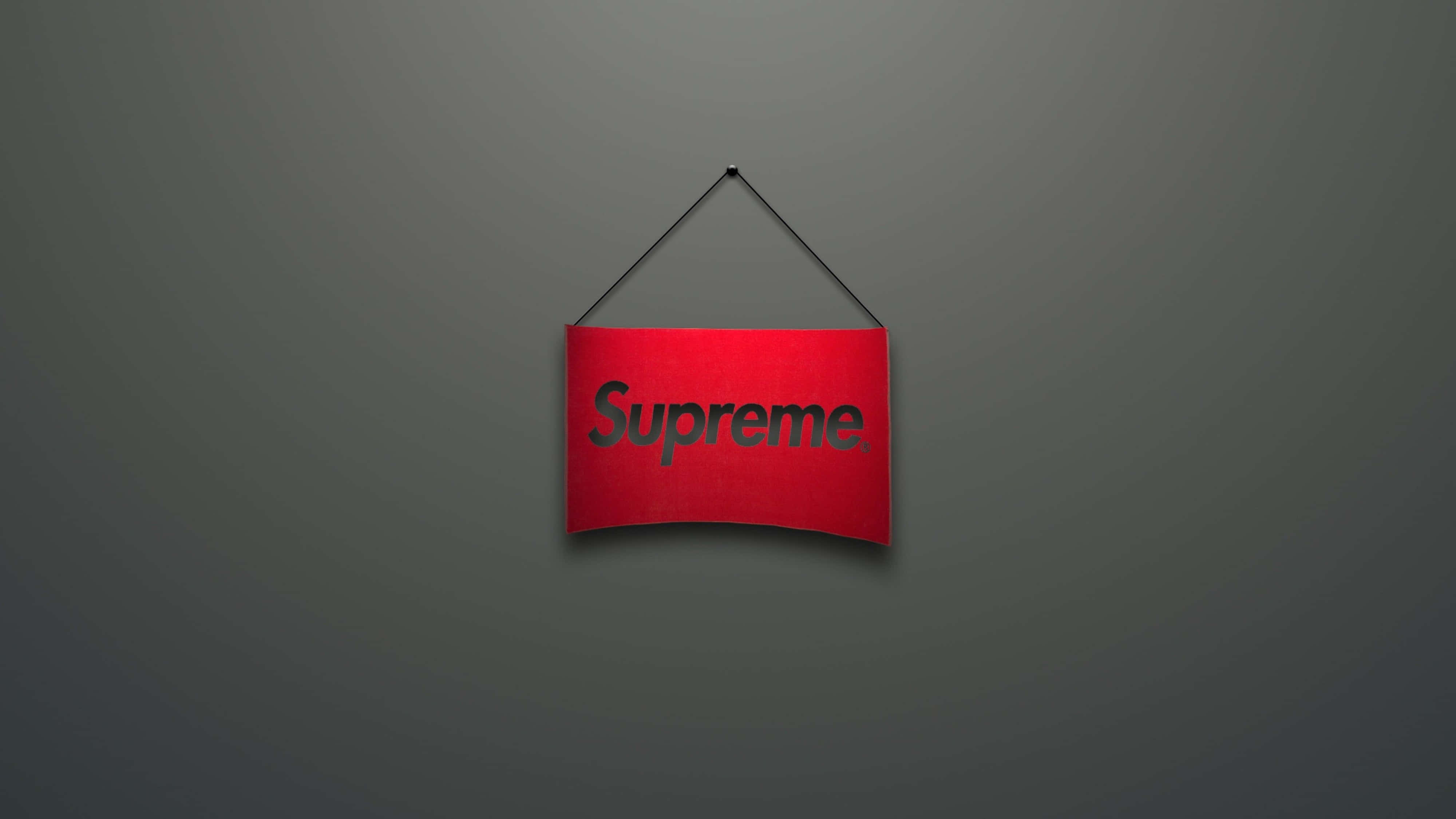 supreme aesthetic 桌布 壁紙 — 一個紅色Supreme標誌牌掛在柔和灰色漸變牆的中心，光線柔和。
