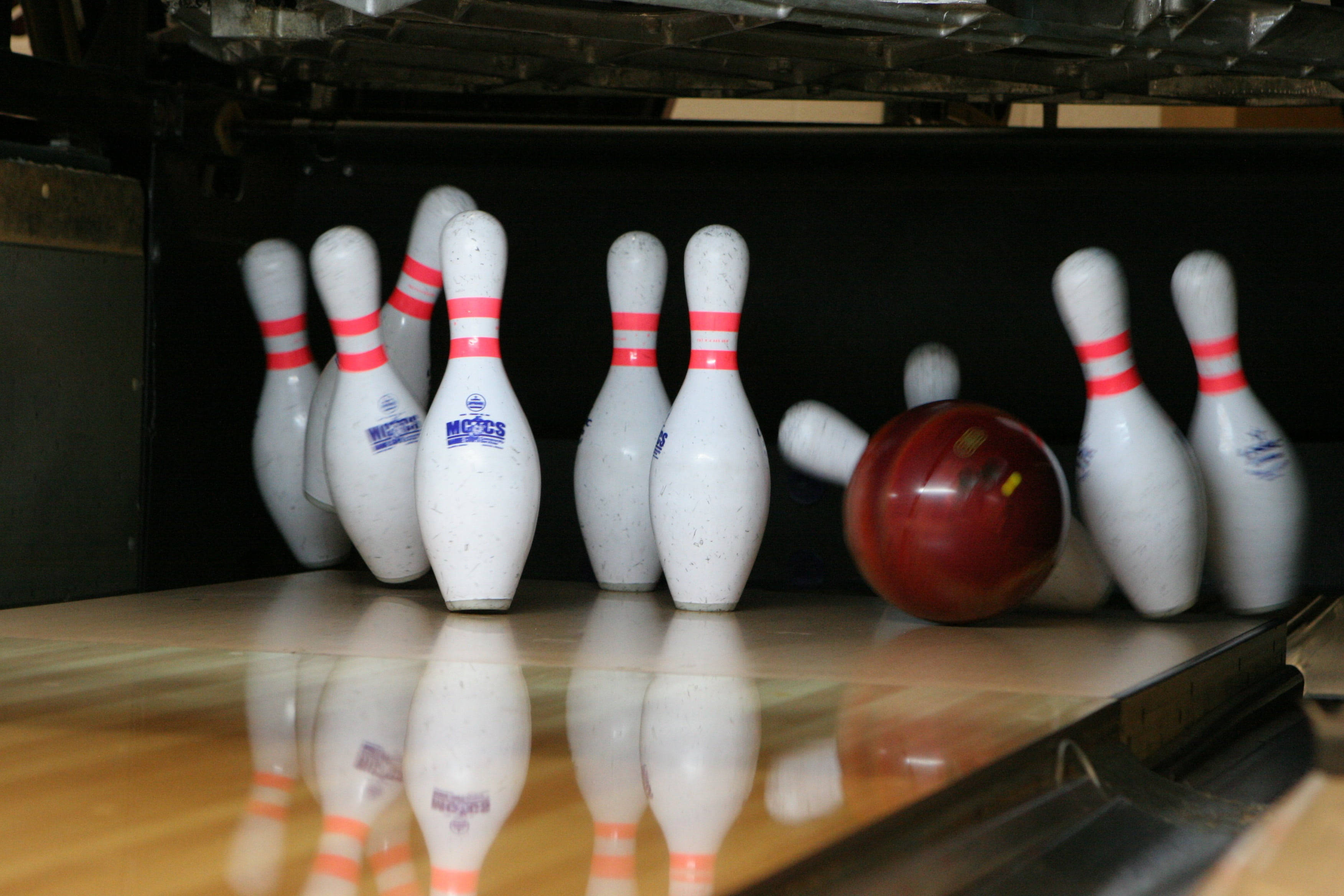Bowling 桌布 壁紙 — 一個紅色保齡球在昏暗燈光下，放在光亮的木製球道上，旁邊是帶有紅色條紋的白色倒下球瓶。