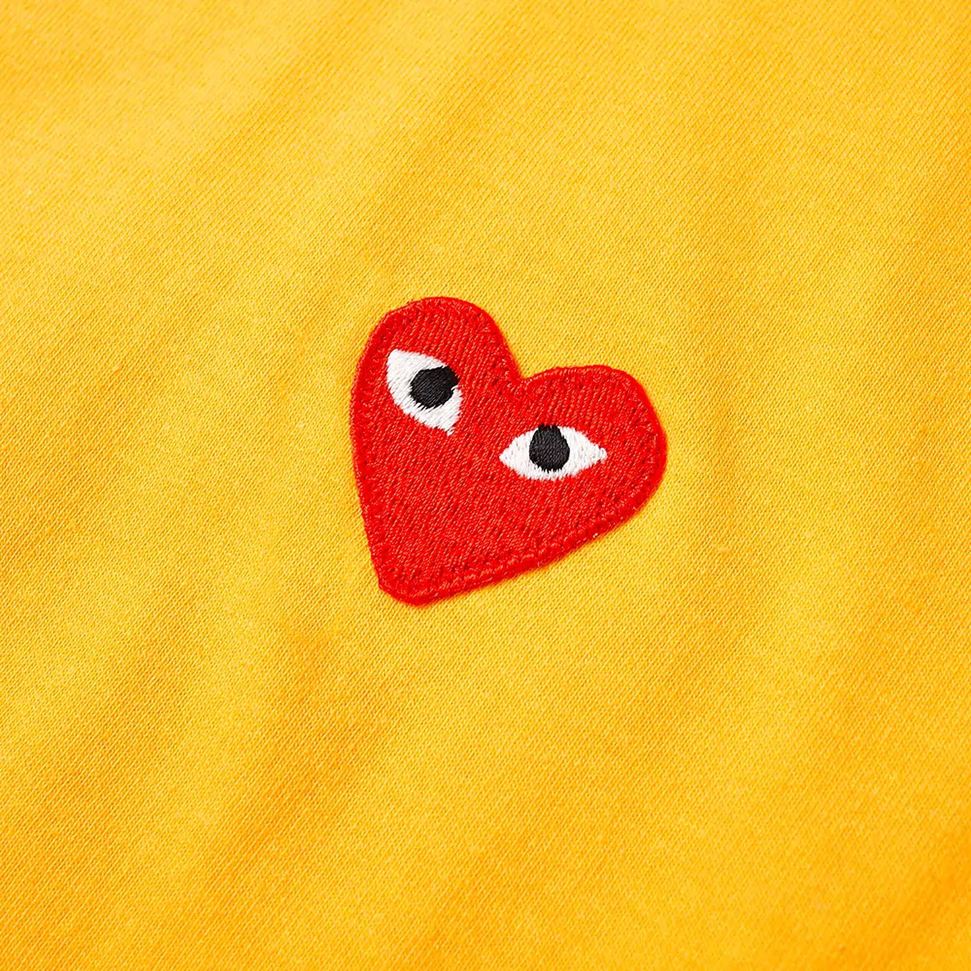 cdg 桌布 壁紙 — 一個紅色刺繡心形，上面縫有兩個白色眼睛，位於有紋理的黃色布料上。