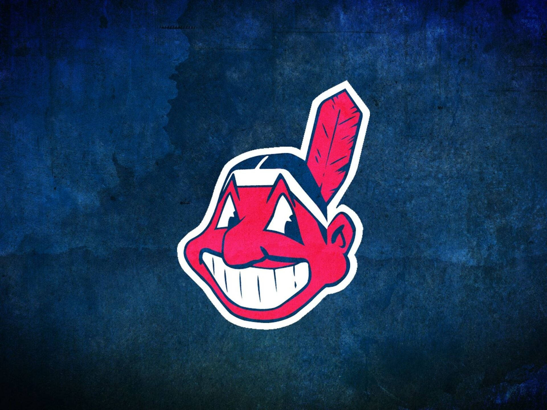 Cleveland Indians 桌布 壁紙 — 一個紅色卡通美洲原住民吉祥物頭像，帶有一根羽毛，背景為紋理深藍色。