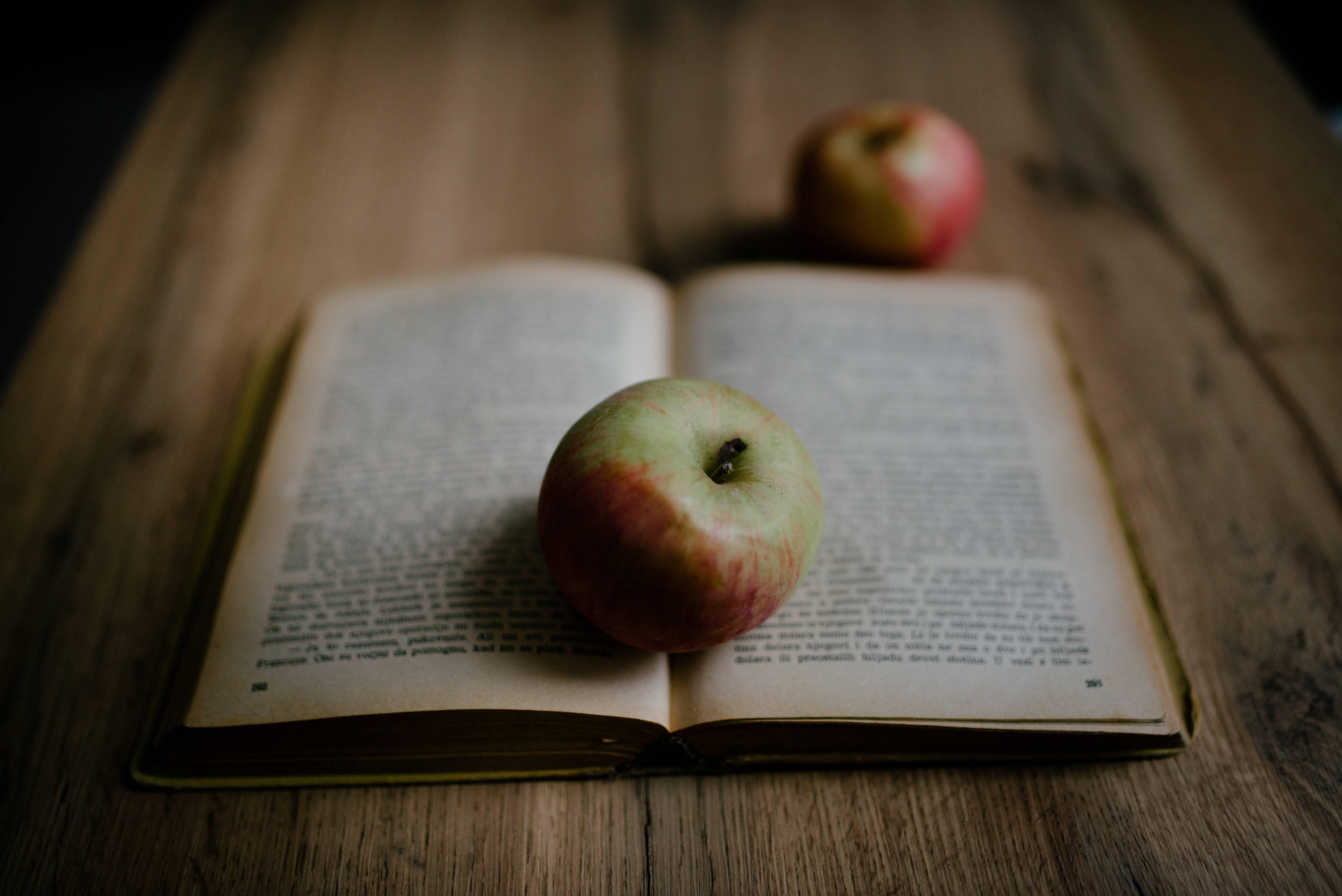 Fruit 桌布 壁紙 — 一個紅色和綠色的蘋果放在一本打開的書上，書放在質樸的木桌上，背景有另一個模糊的蘋果。