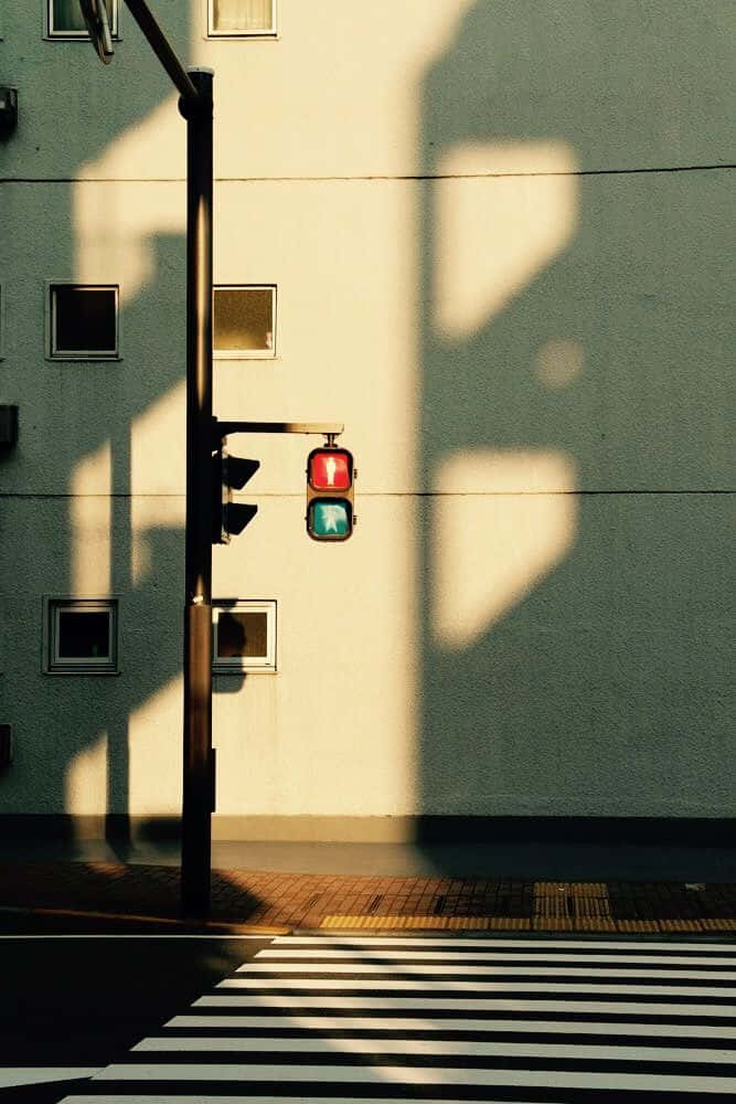 Minimalist Photography 桌布 壁紙 — 一個紅色和綠色的行人交通燈在陽光普照的城市建築牆壁上，在斑馬線旁邊投下長長的陰影。