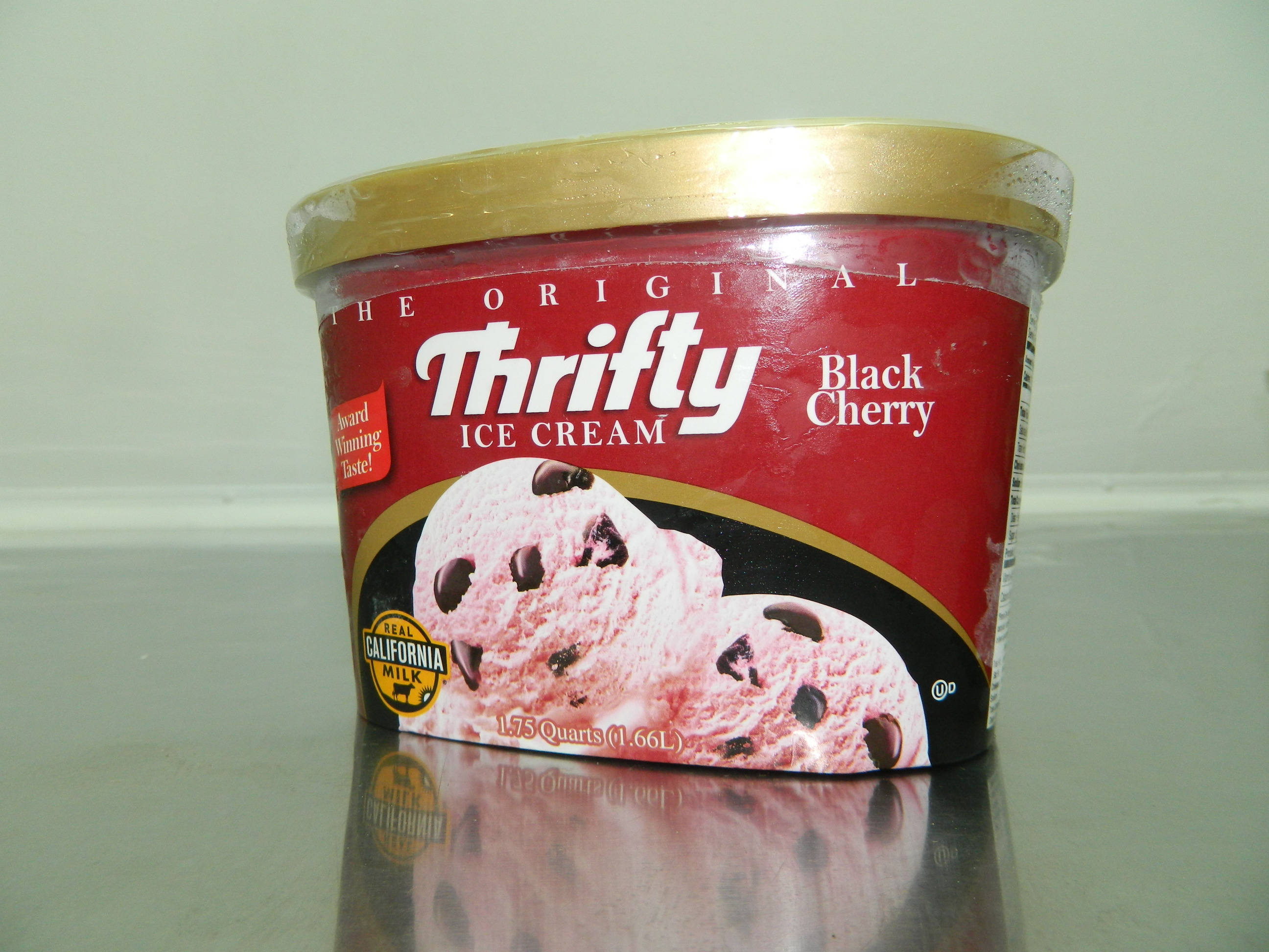 Ice Cream 桌布 壁紙 — 一個紅色和金色的Thrifty Black Cherry冰淇淋桶，內含巧克力塊，放在反光的檯面上。