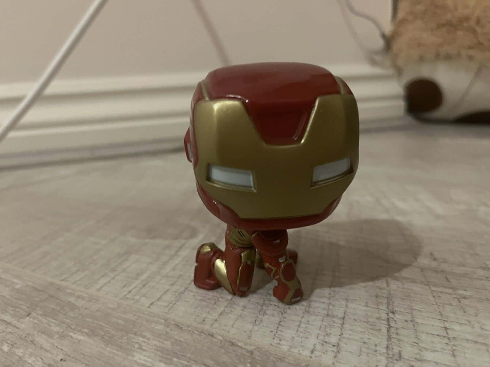 Iron Man Pop Figures 桌布 壁紙 — 一個紅色和金色的鋼鐵人 Funko Pop! 人偶跪在淺色木地板上，背景模糊。