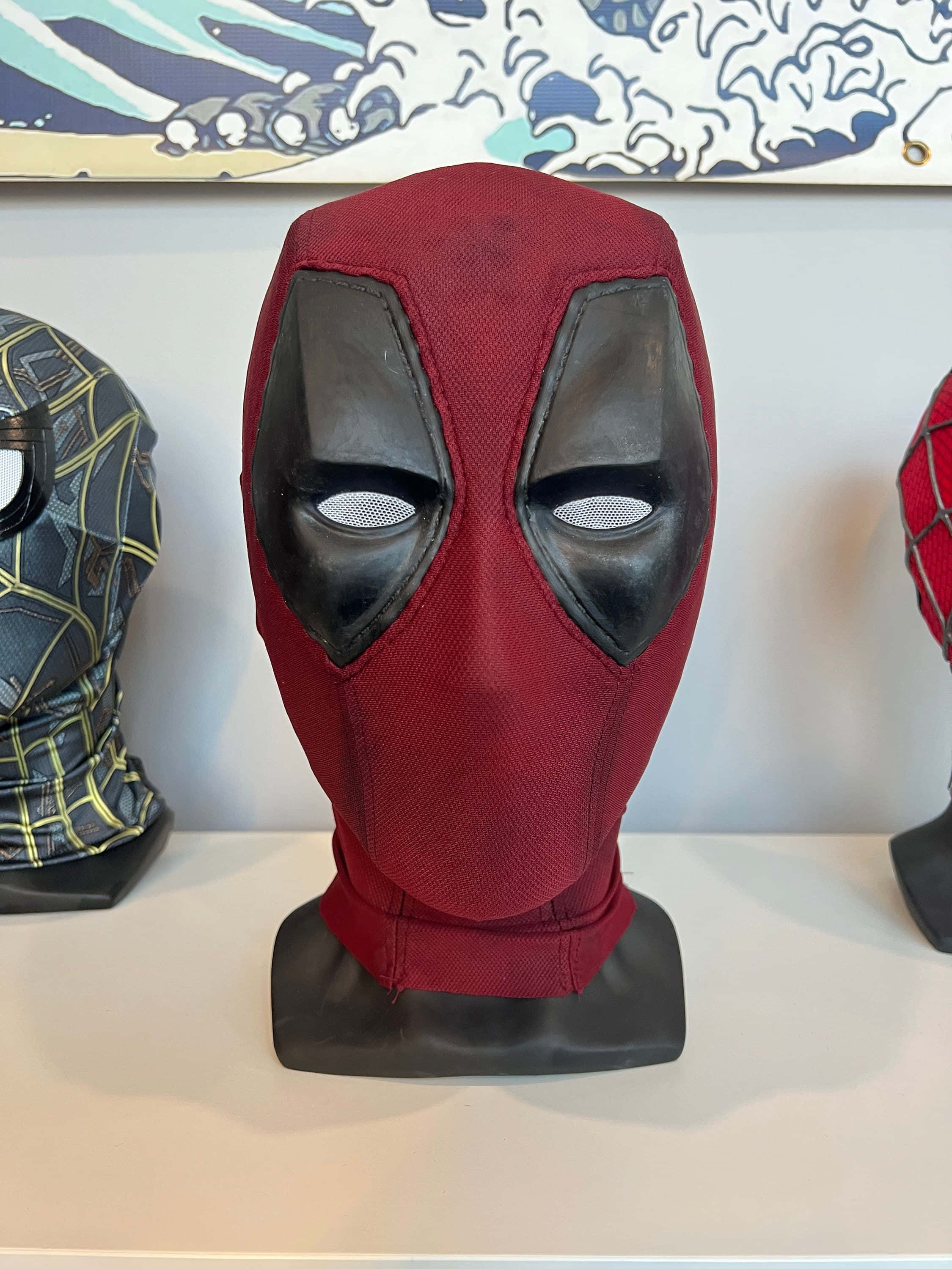 Deadpool Mask 桌布 壁紙 — 一個紅色和黑色的死侍面具陳列在架子上的展示架上，與其他超級英雄面具一起。