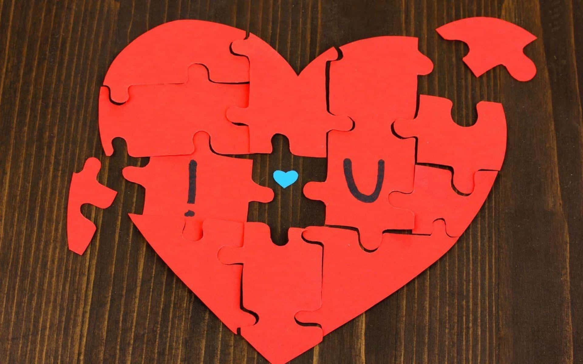 Puzzle 桌布 壁紙 — 一個紅色心形拼圖，缺少的拼塊拼出「I U」，中間有一個藍色小愛心，放在深色木質表面上。