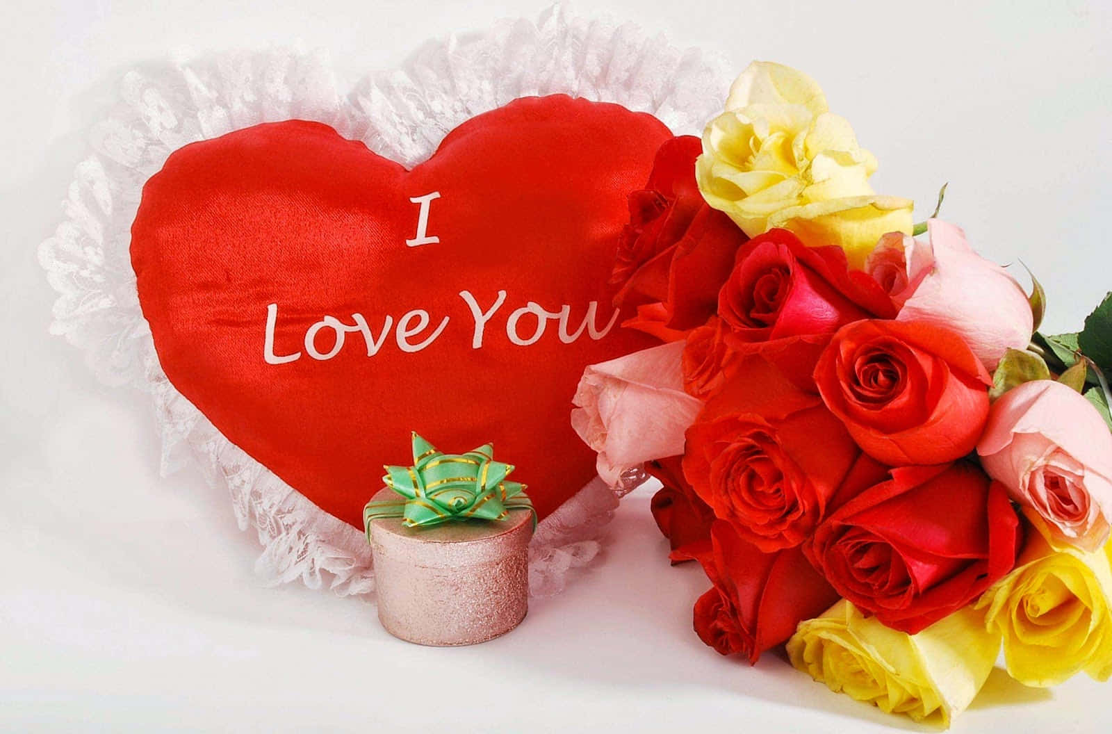 love you 桌布 壁紙 — 一個紅色心形枕頭，上面有 I Love You 字樣，旁邊放著一束紅、粉紅和黃色的玫瑰，以及一個小禮物盒。