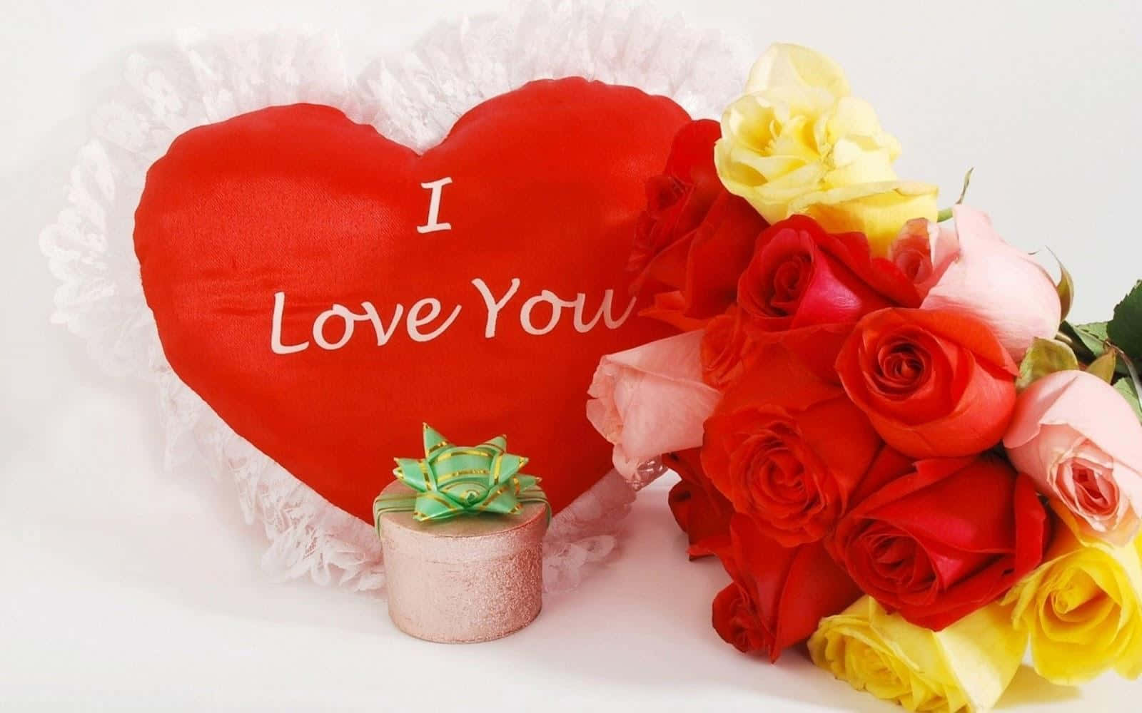 Heart Shape 桌布 壁紙 — 一個紅色心形枕頭，上面有 I Love You 字樣，旁邊放著一束鮮豔的紅、粉紅和黃色玫瑰，以及一個小禮物盒。