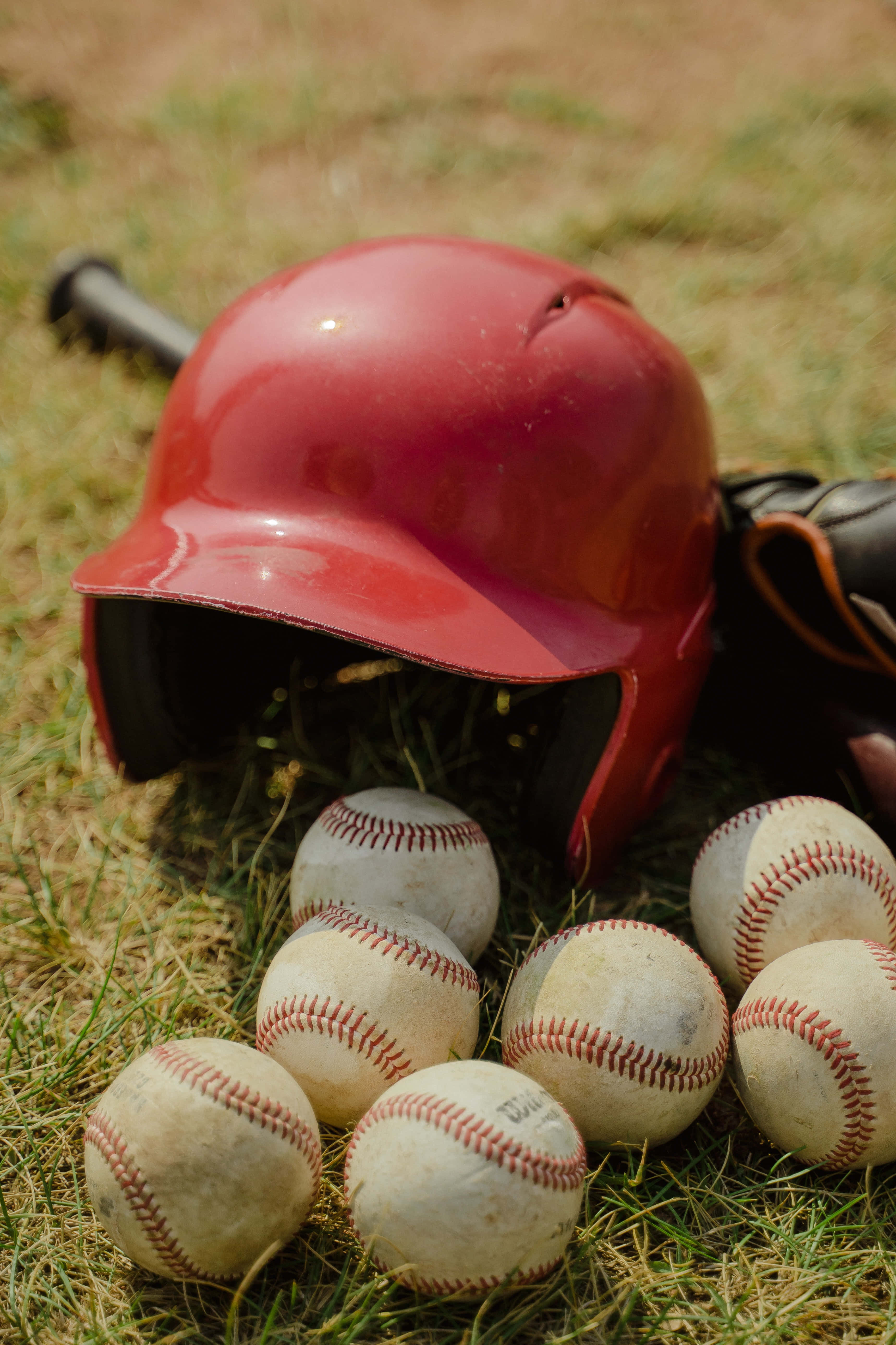 baseball bat 桌布 壁紙 — 一個紅色棒球頭盔和磨損的球放在陽光照耀的草地上，旁邊有球棒和手套。