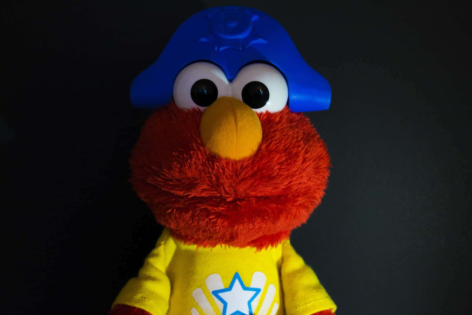 Elmo 桌布 壁紙 — 一個紅色毛絨Elmo公仔的特寫，戴著藍色警察帽和黃色星星衫。