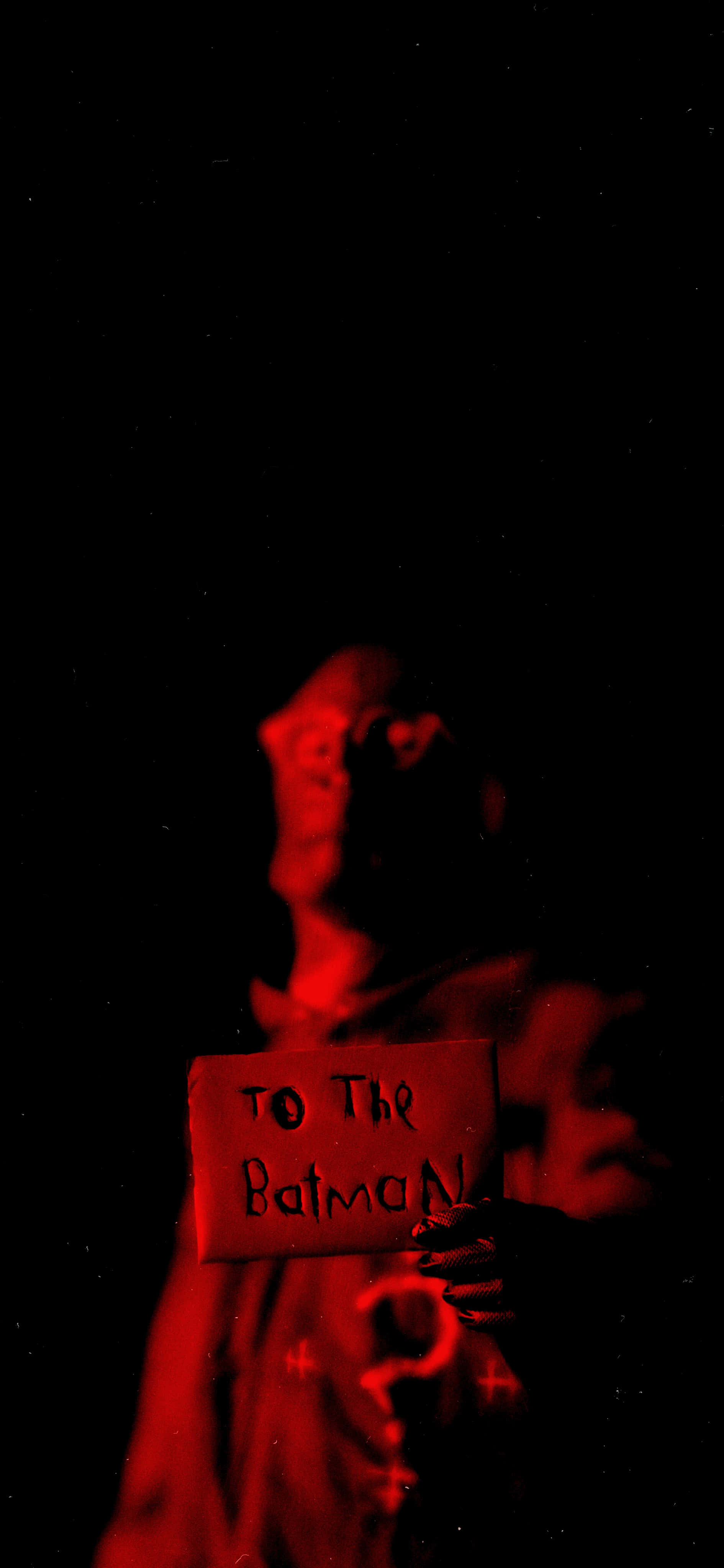The Riddler 2022 桌布 壁紙 — 一個紅色燈光下的陰影人物，在黑色背景前舉著一個寫有「to the batman」的標牌。