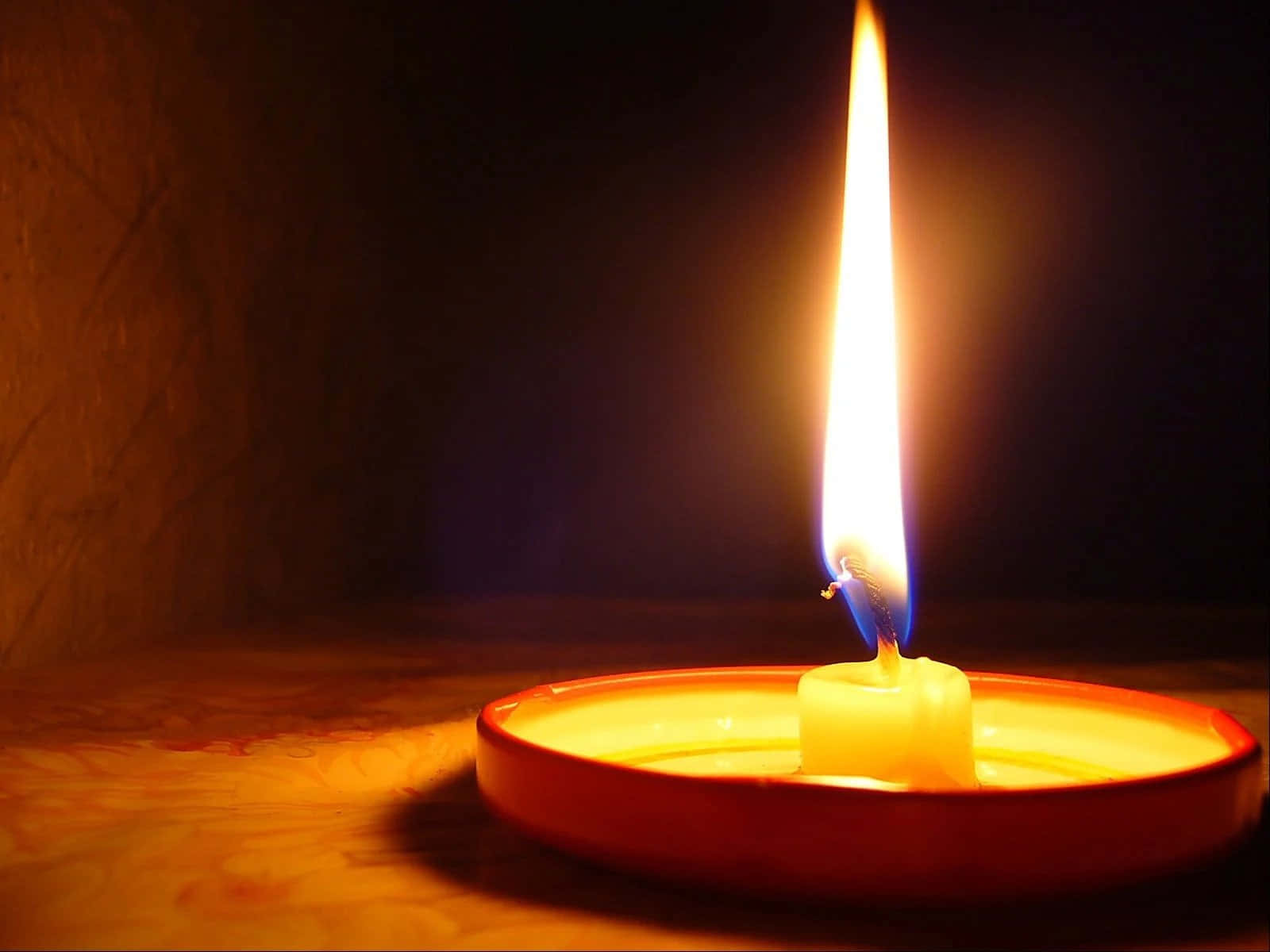 Candle Light 桌布 壁紙 — 一個紅色燭台上的單支點燃蠟燭，在黑暗的紋理背景上投射出溫暖的金色光芒。