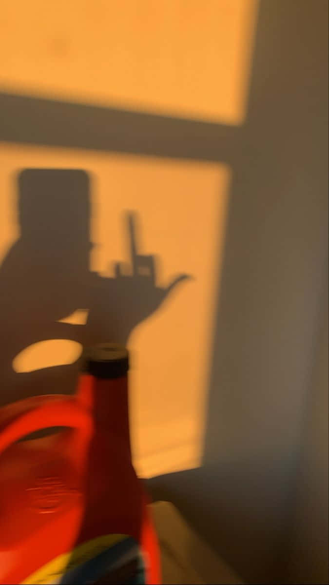 Middle Finger 桌布 壁紙 — 一個紅色瓶子在溫暖照明的牆上投射出一個人拿著電話的清晰影子。