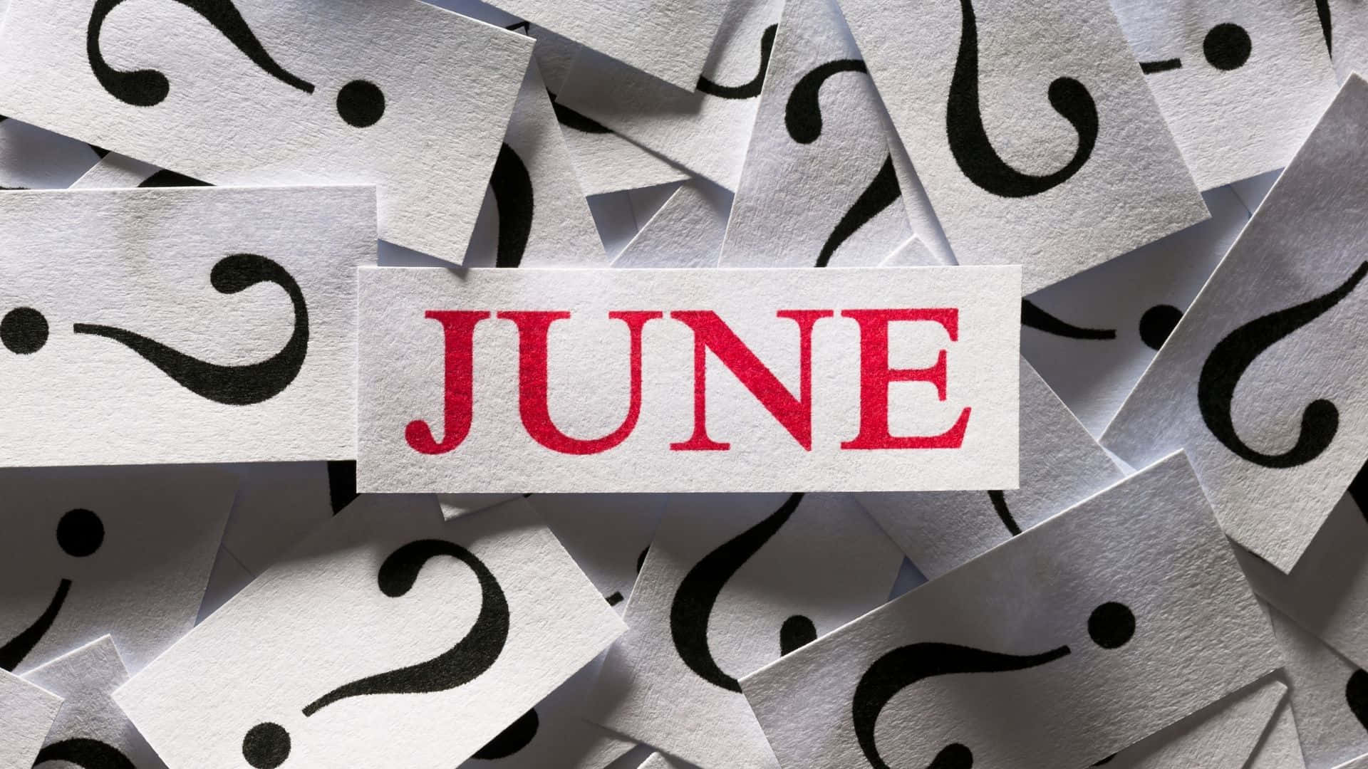 June 桌布 壁紙 — 一個紅色的「JUNE」標籤放在散落的白色卡片上，卡片上有黑色問號，象徵對該月的不確定或好奇。